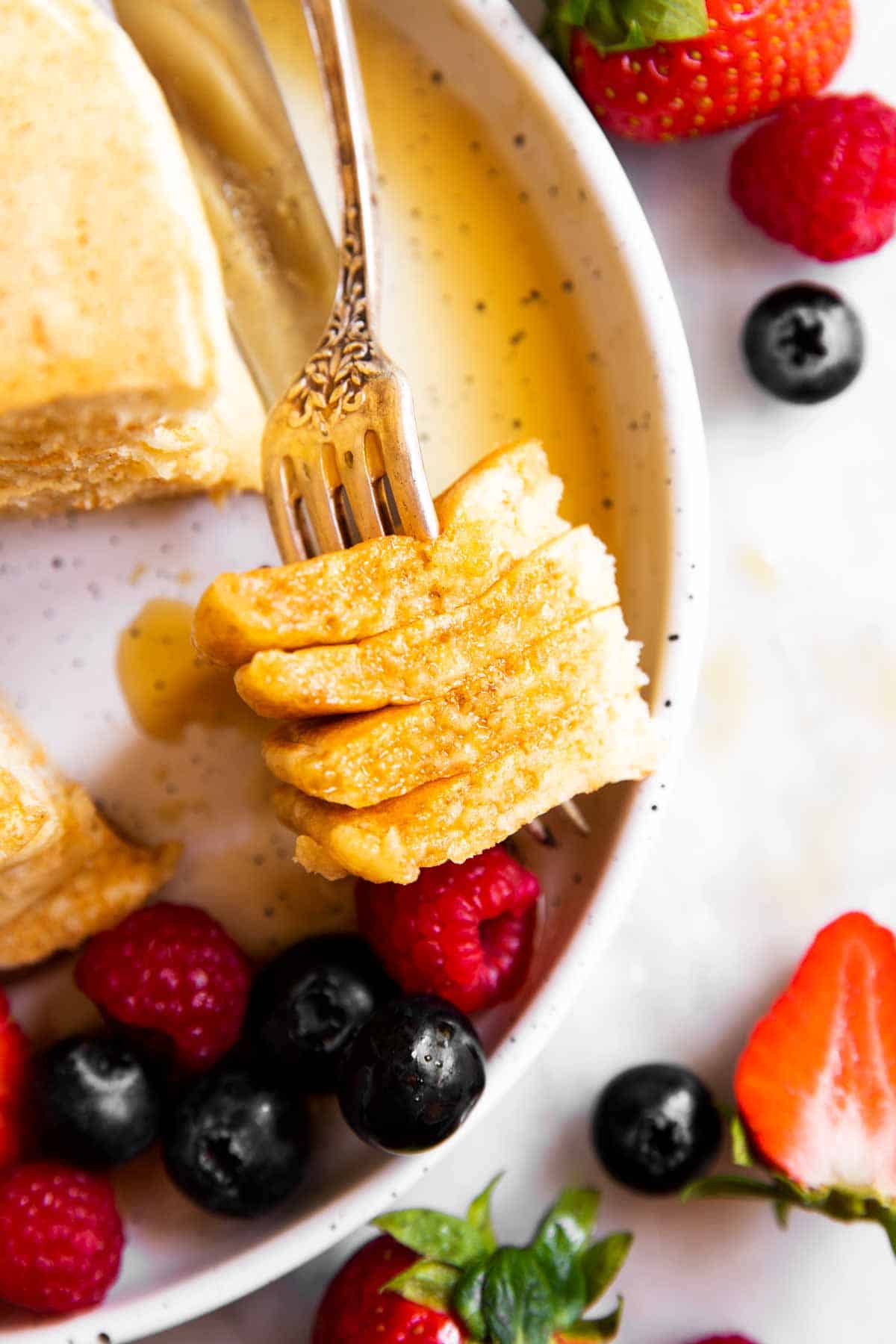 fork with cut pancakes on white plate with syrup and berries
