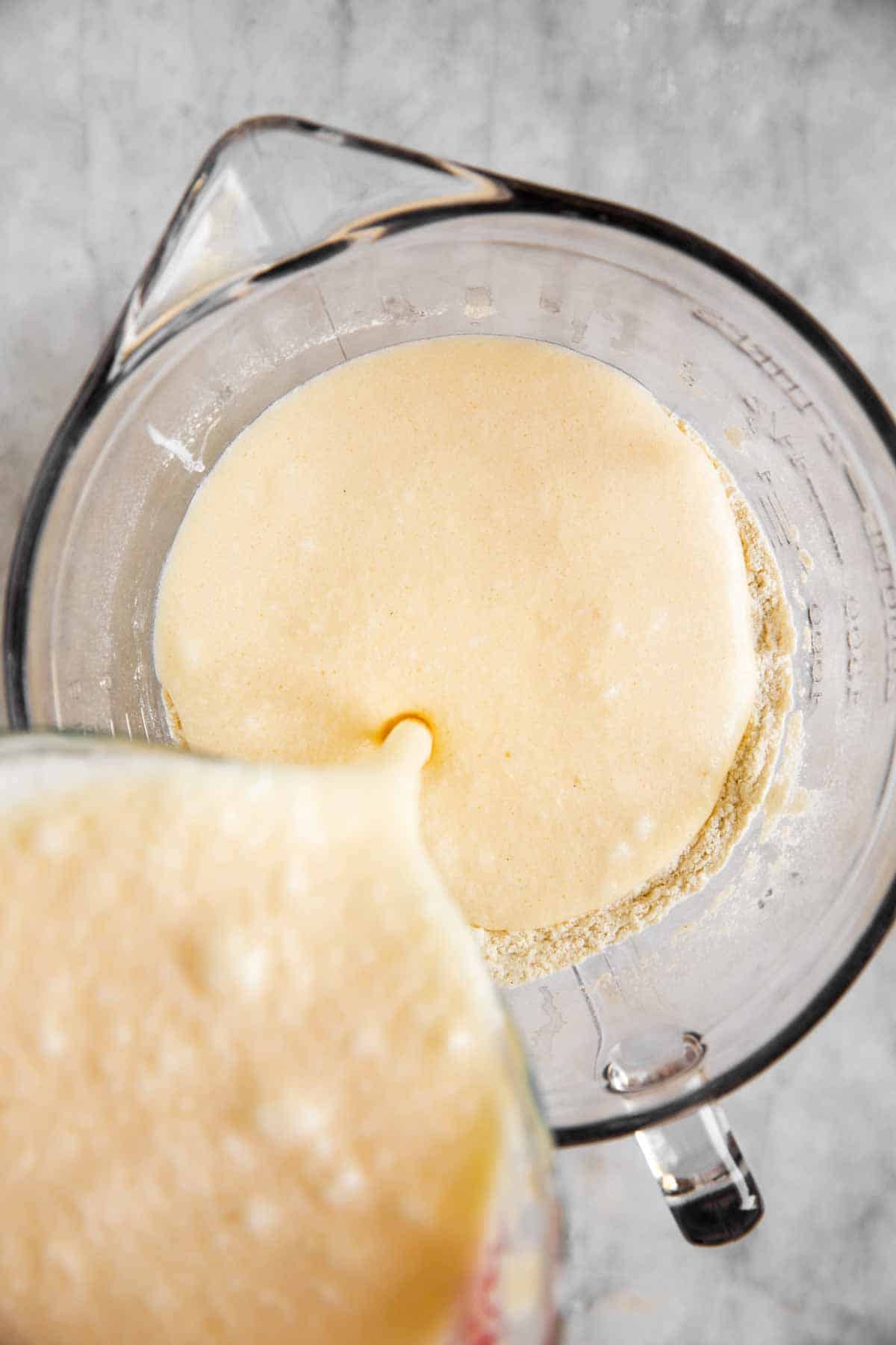 pouring wet ingredients into glass bowl with dry ingredients for pancake batter