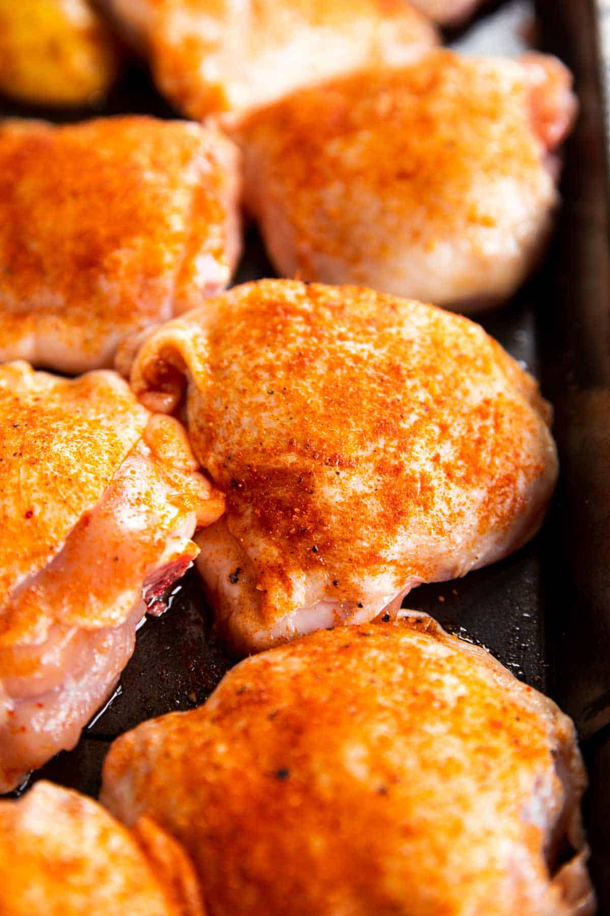 close up photo of seasoned chicken thighs on black sheet pan