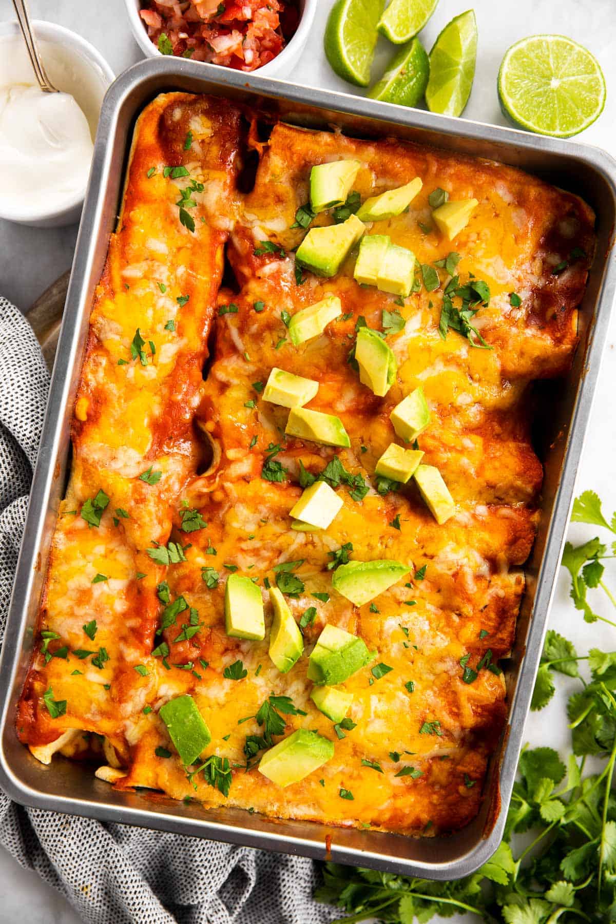 overhead view of chicken enchiladas in casserole dish, topped with cilantro and avocado