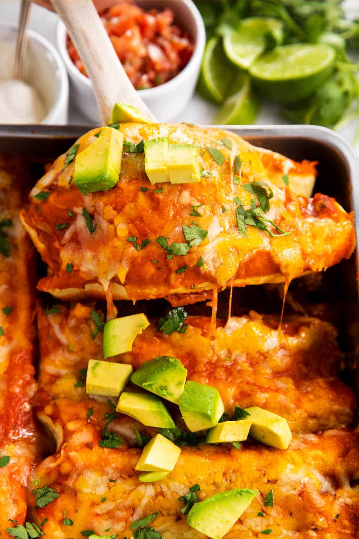 lifting two chicken enchiladas out of casserole dish with wooden spoon