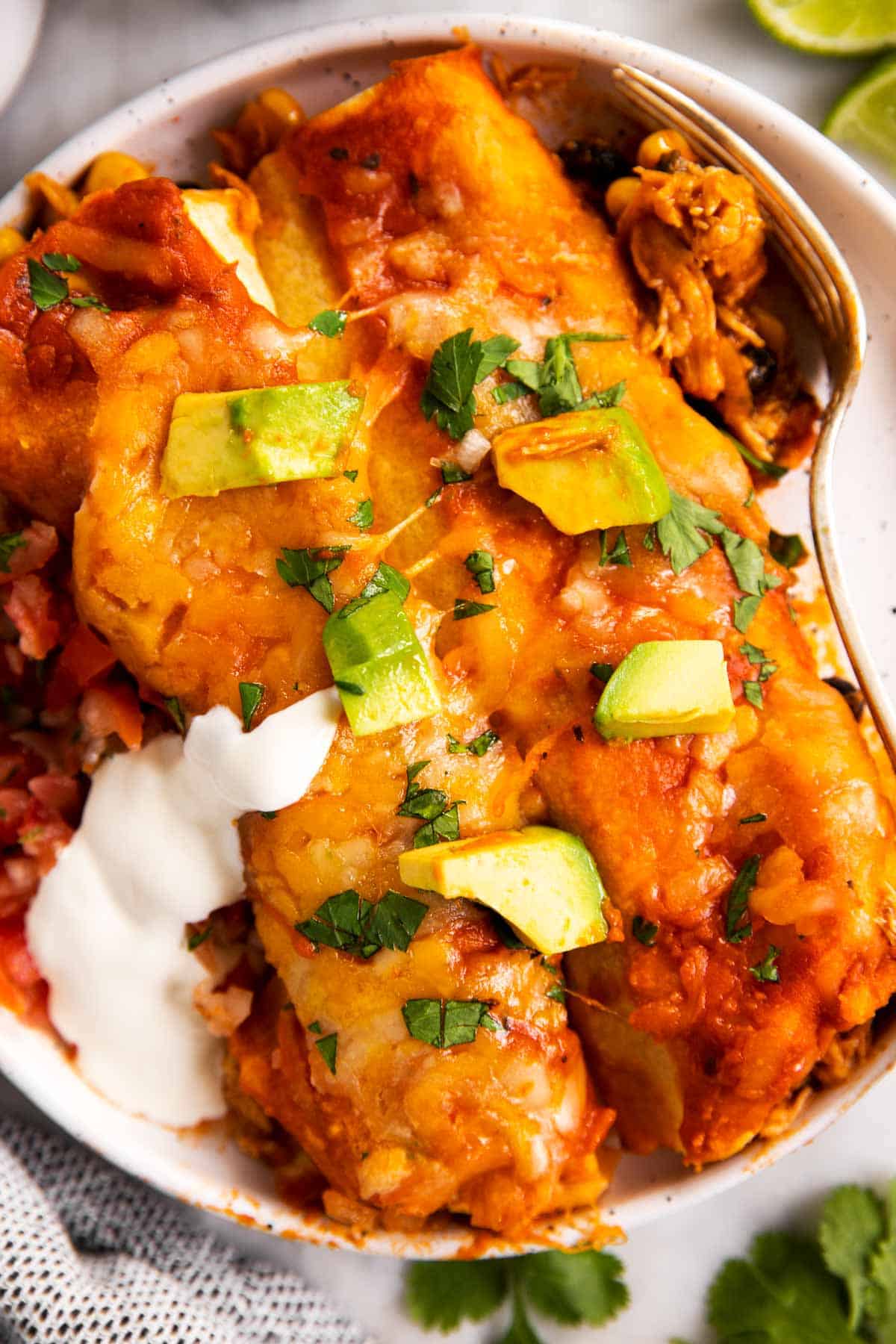 overhead view of two chicken enchiladas on white plate with avocado and sour cream