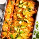 overhead view of chicken enchiladas in casserole dish, topped with cilantro and avocado