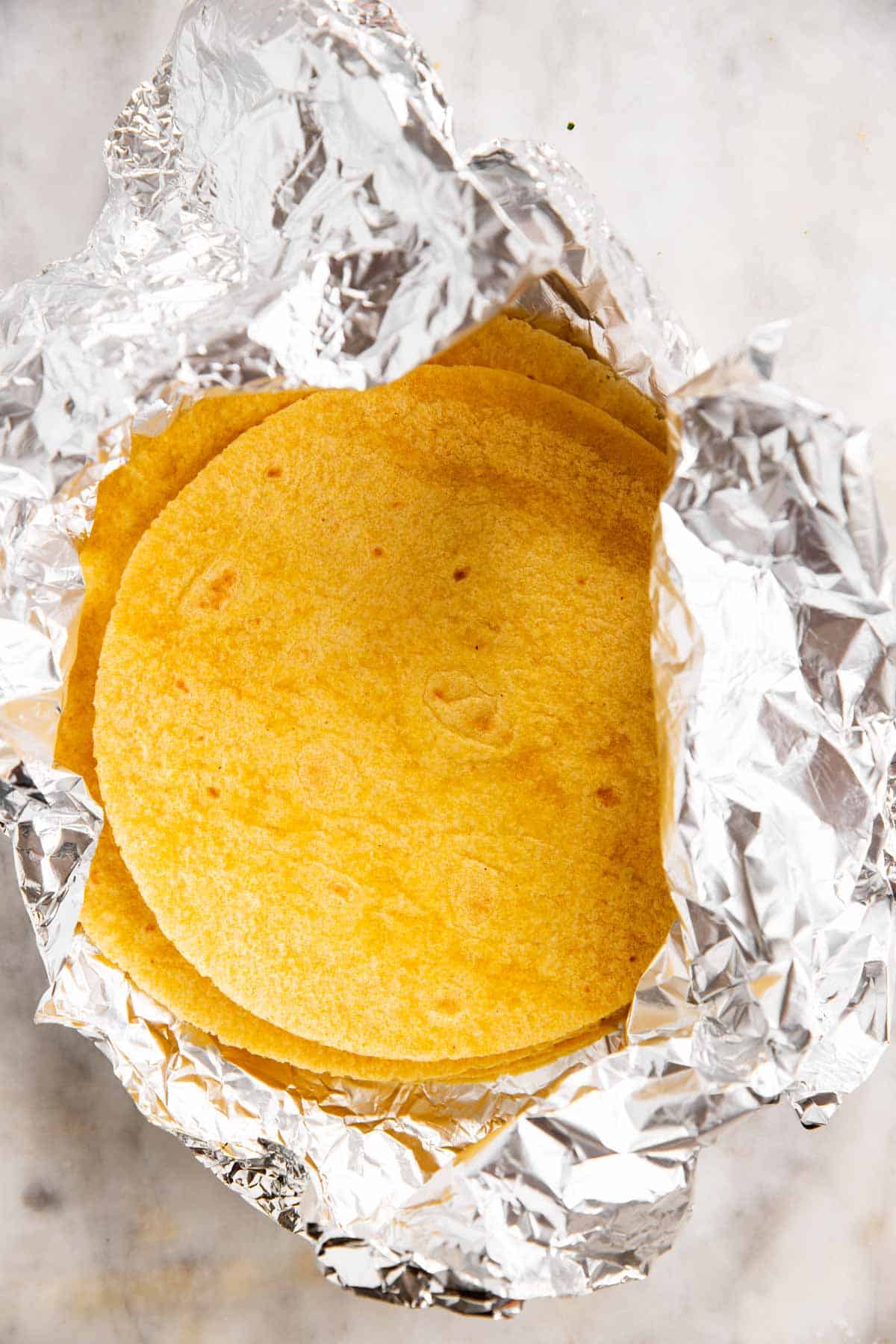 corn tortillas in aluminum foil on marble surface