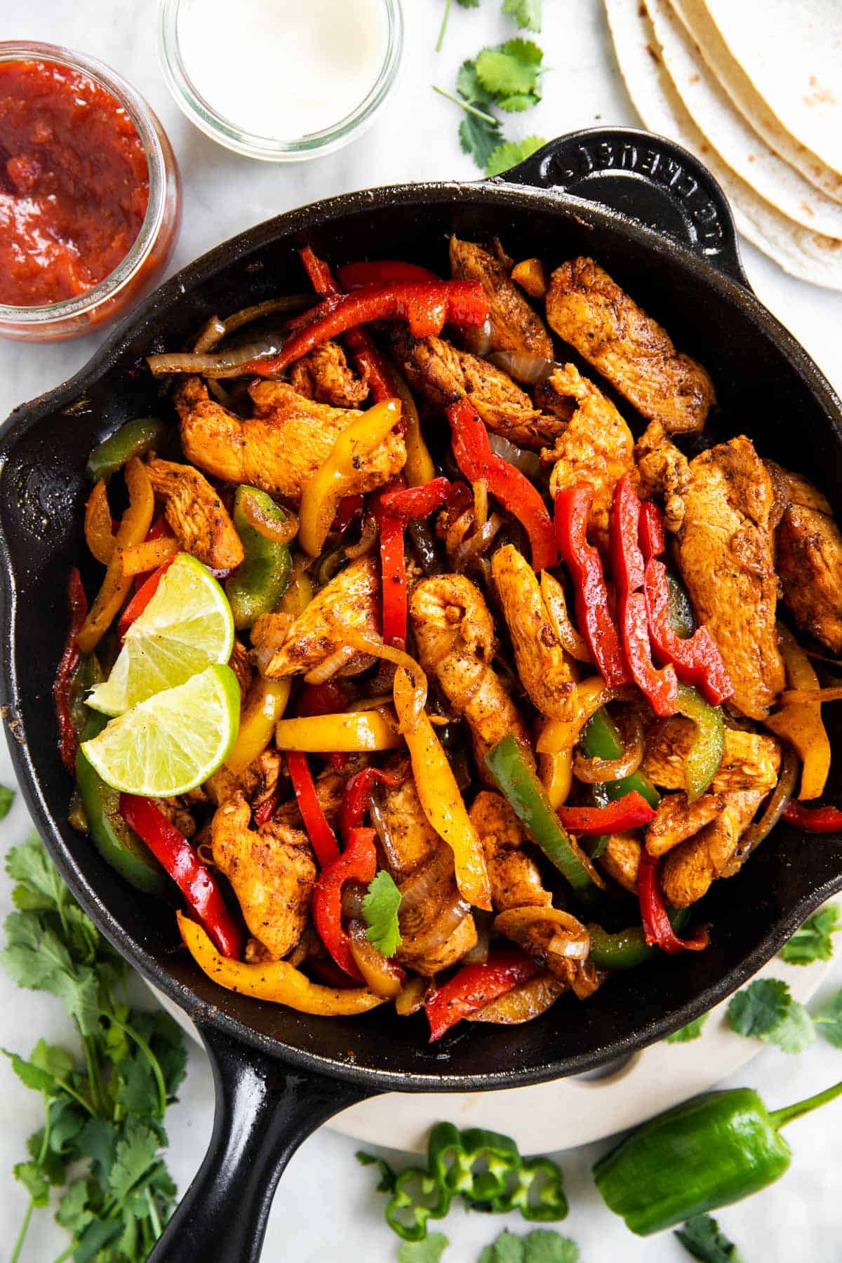 overhead view of chicken fajita filling in black cast iron skillet, surrounded by fajita toppings