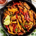 overhead view of chicken fajita filling in black cast iron skillet, surrounded by fajita toppings