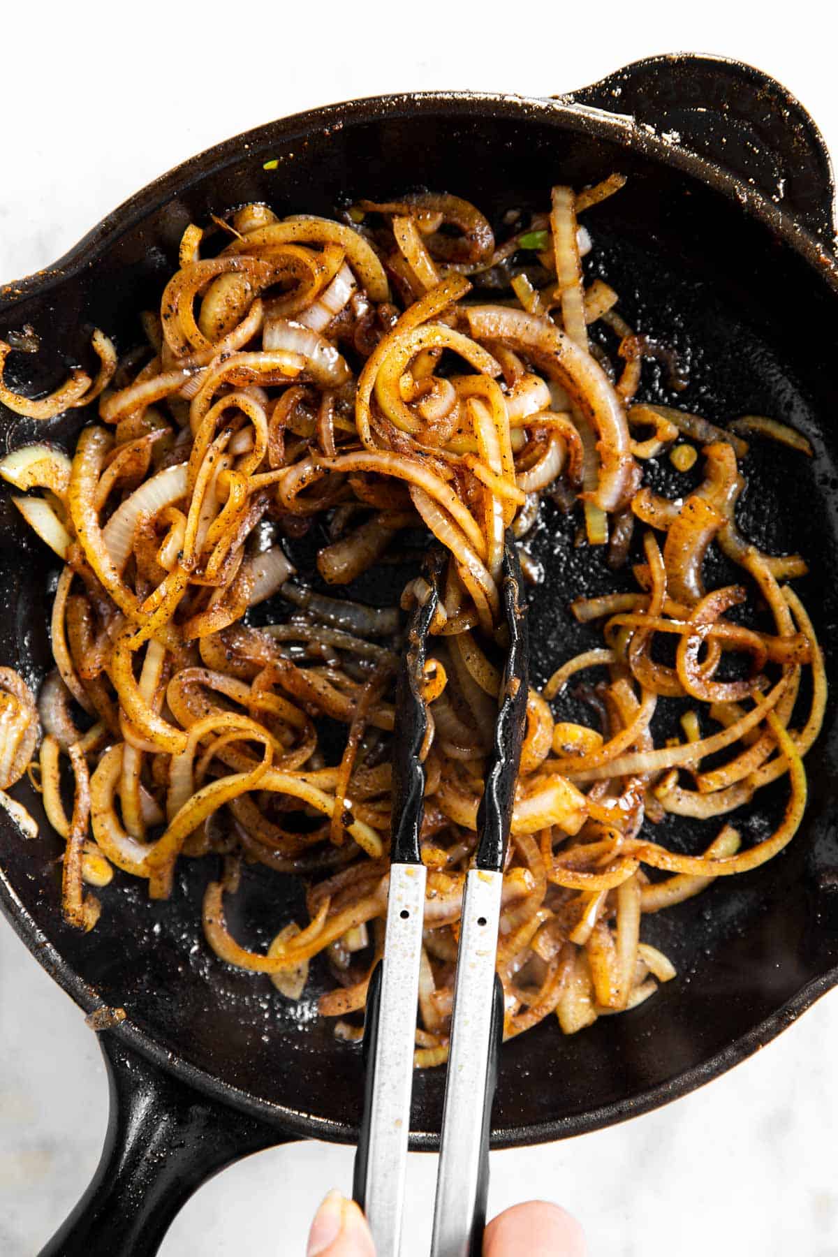cooked onions in black skillet with kitchen tongs