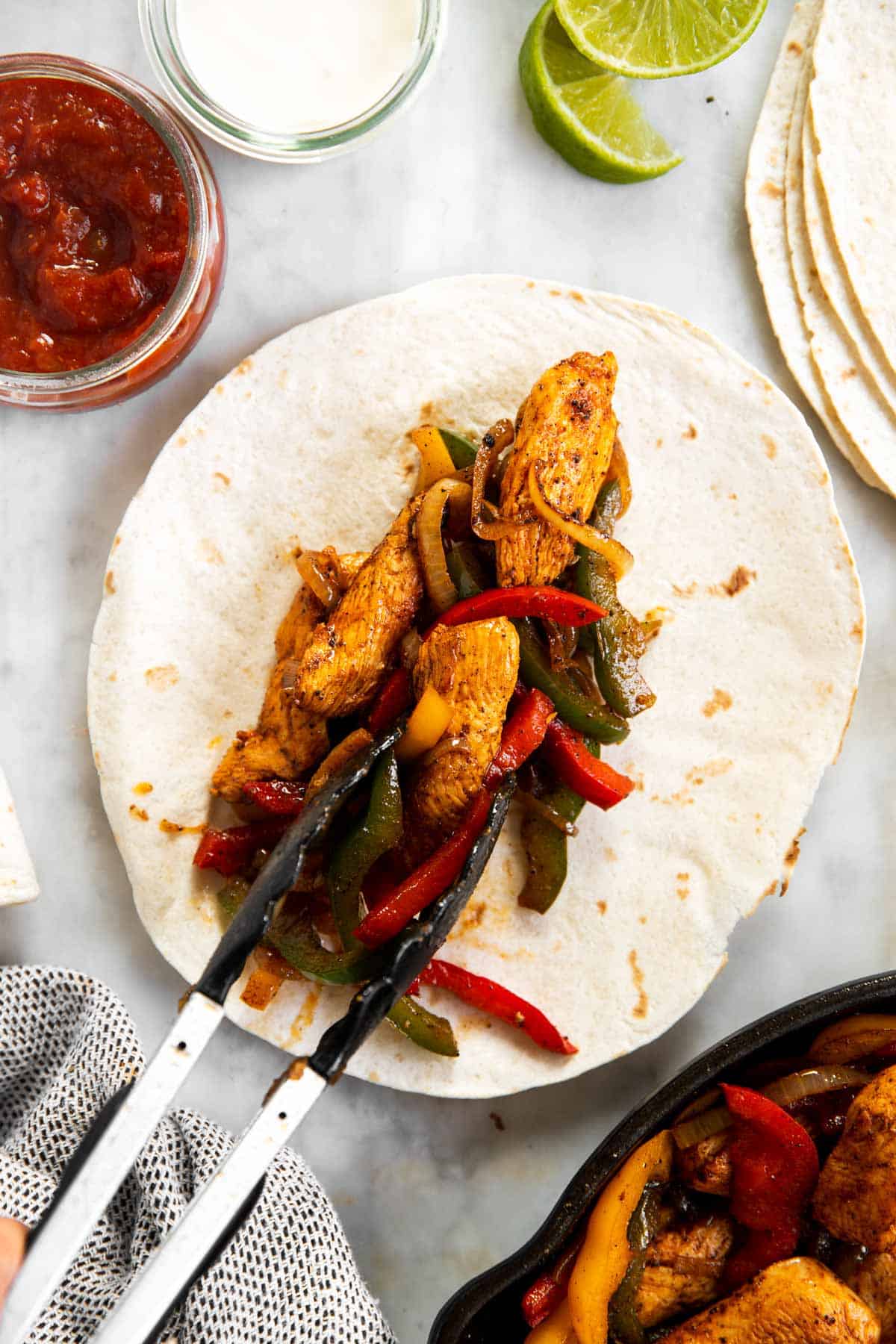chicken fajita filling placed on flour tortilla with kitchen tongs