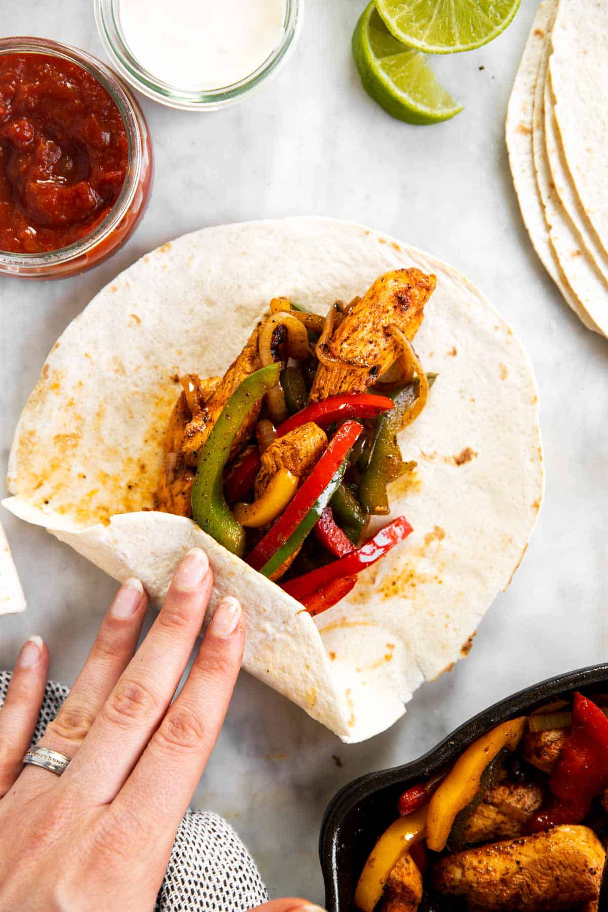 female hand rolling up bottom of flour tortilla over chicken fajita filling