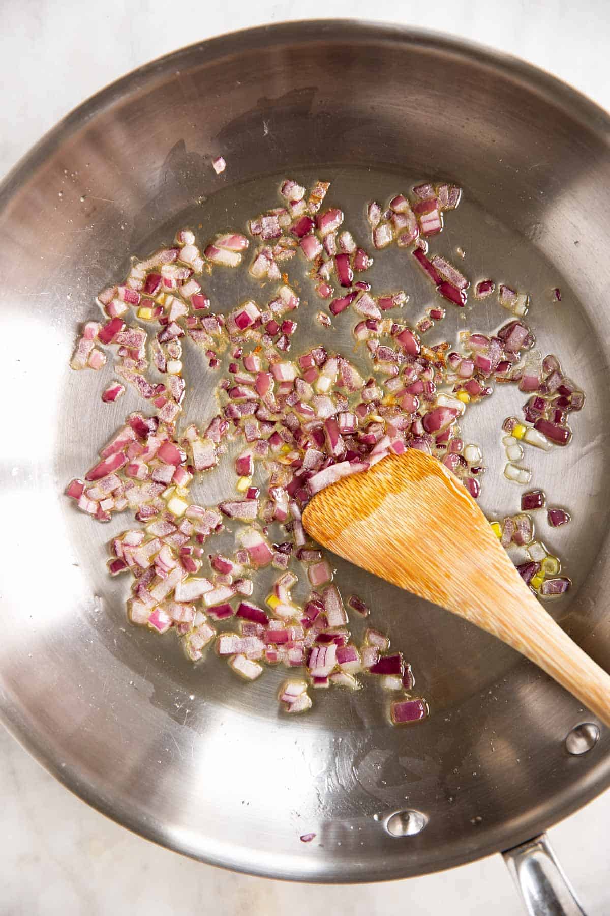 cooked red onion in skillet with wooden spoon