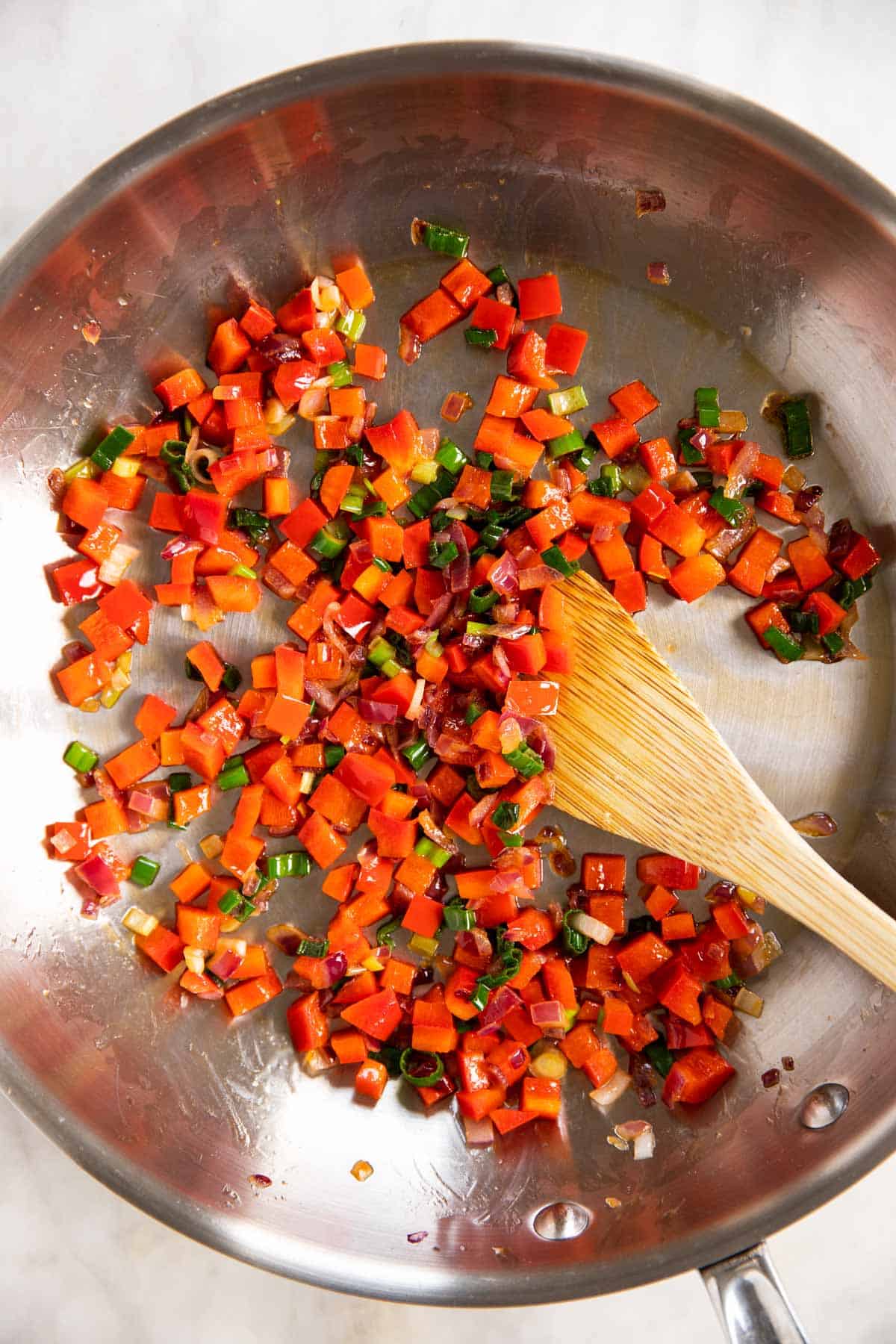 cooked red onion, pepper and green onion in skillet with wooden spoon