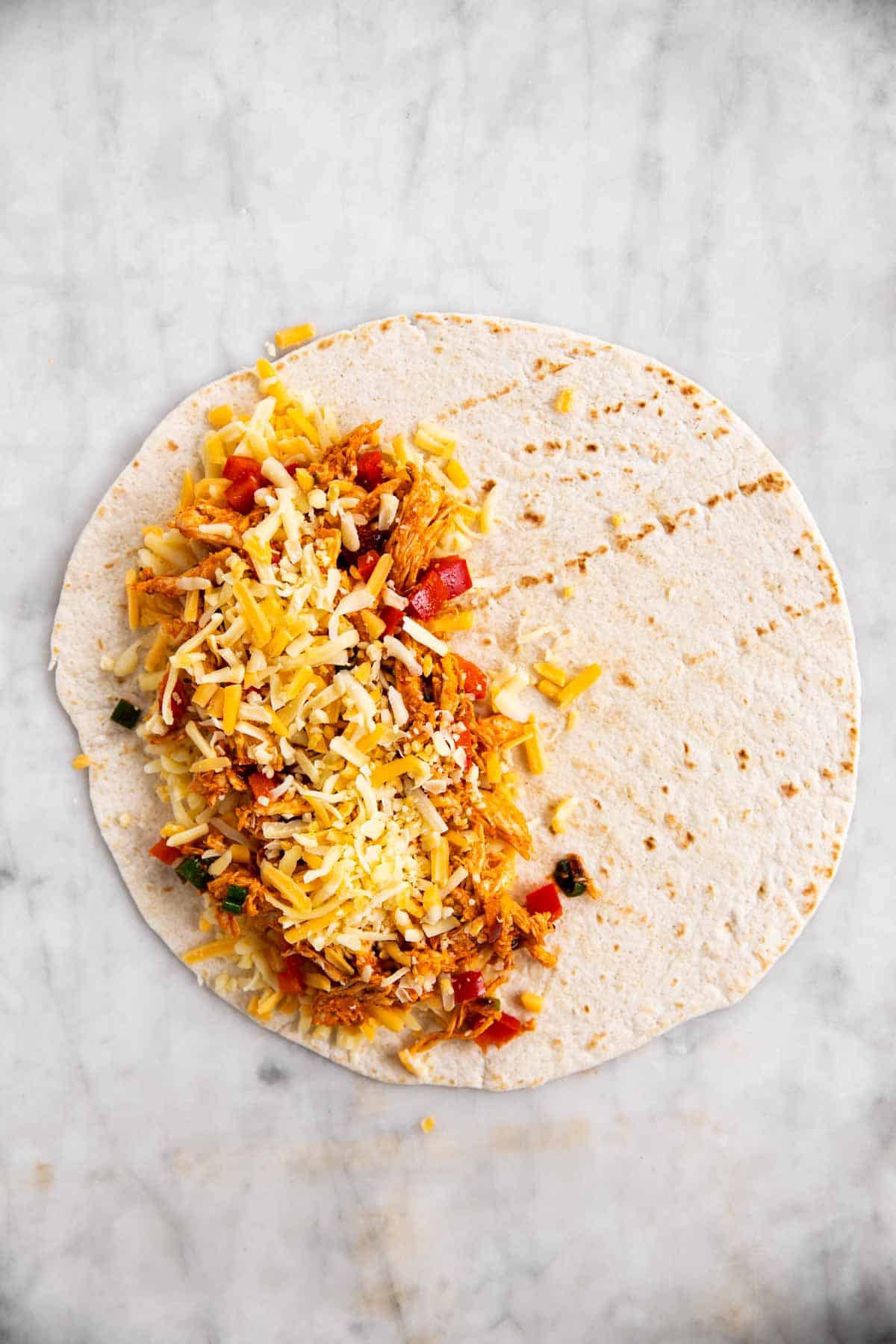 tortilla wrap with chicken quesadilla filling topped with shredded cheese on one half