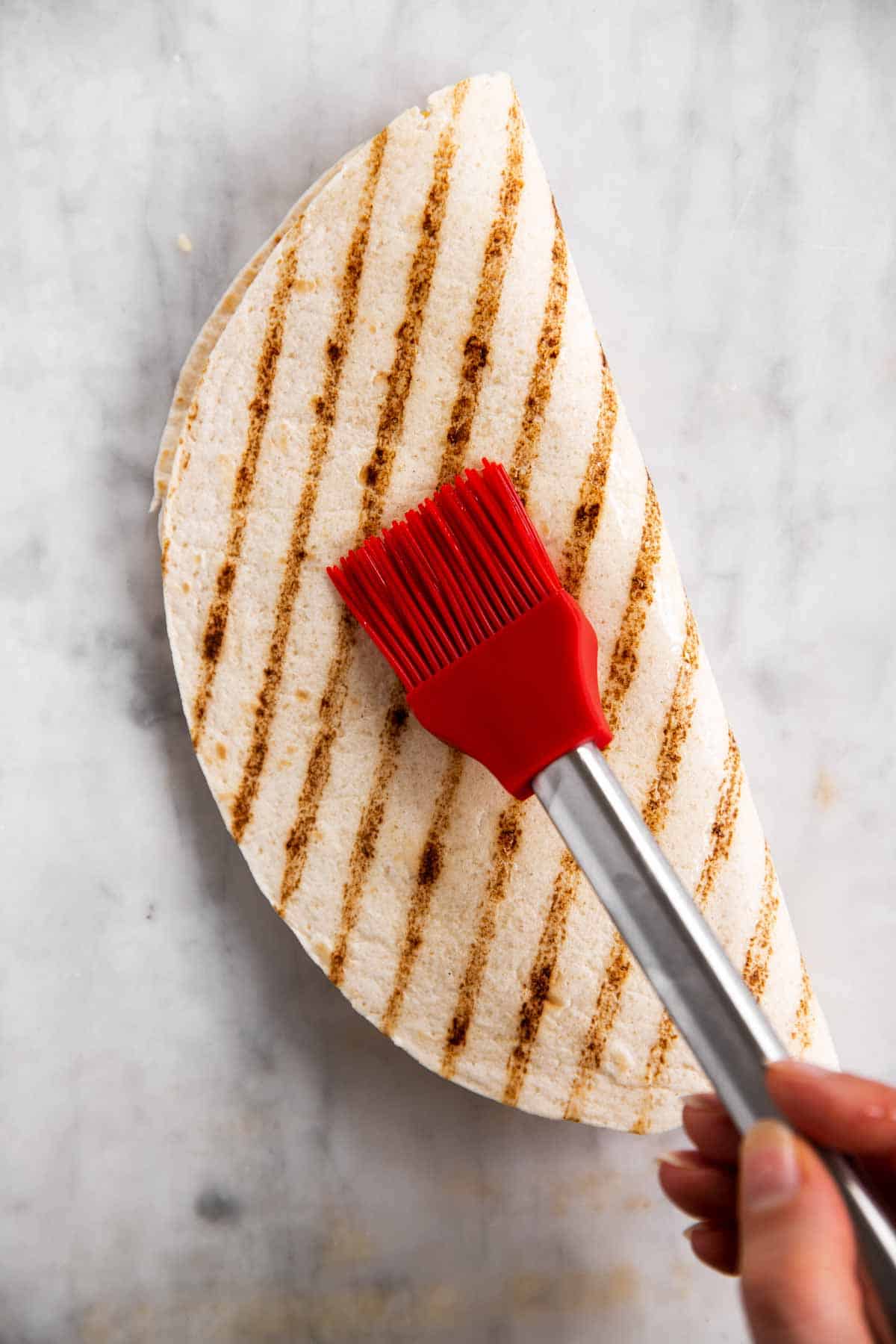 female hand using red pastry brush to brush oil on folded tortilla wrap