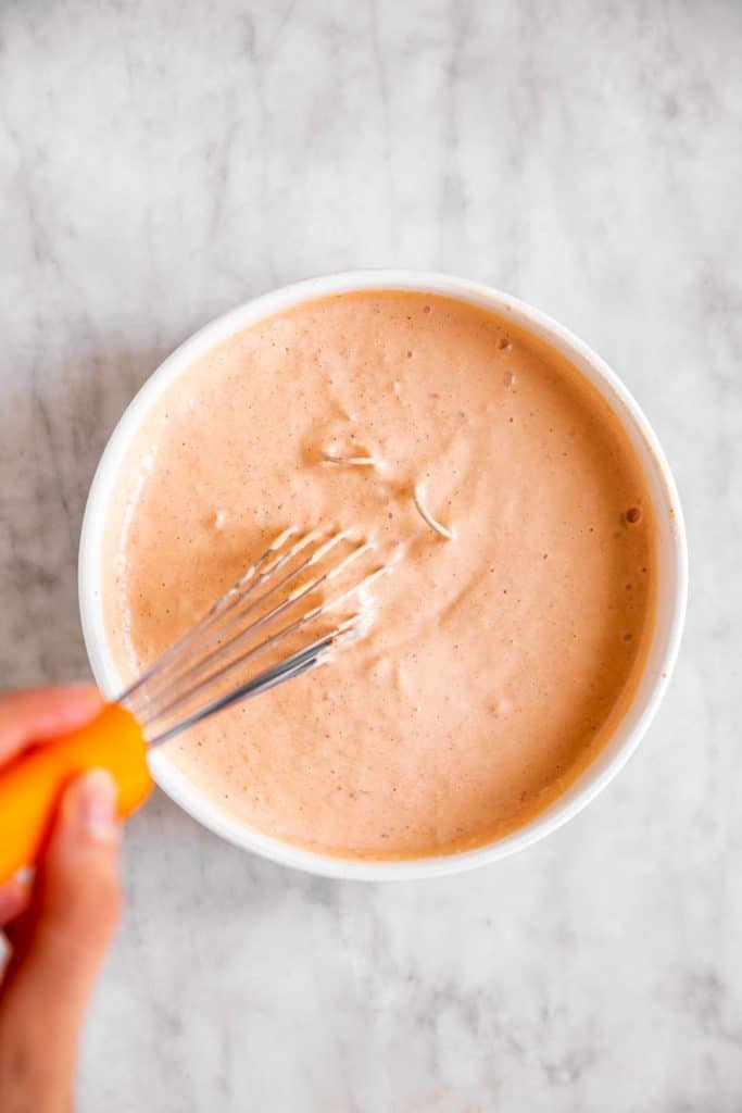 female hand whisking chipotle mayo in white bowl