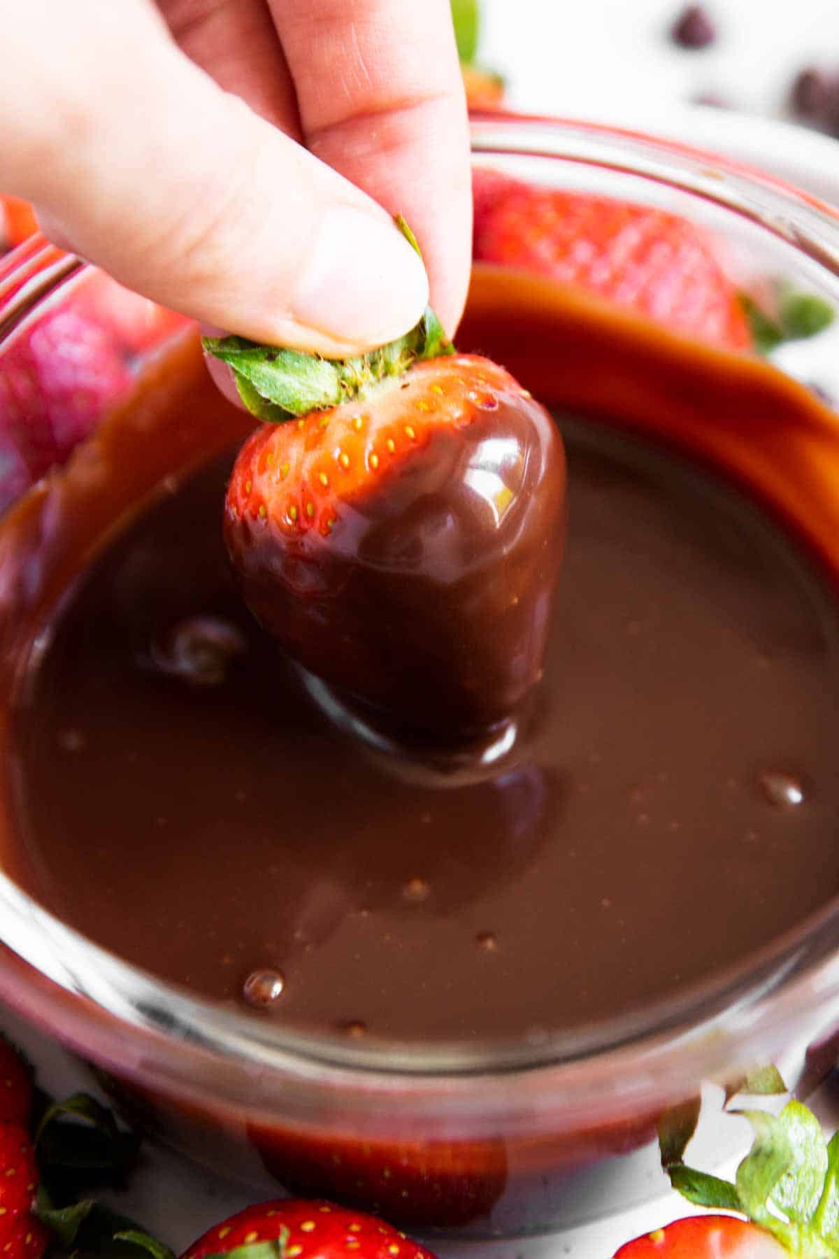 female hand dipping strawberry in chocolate sauce