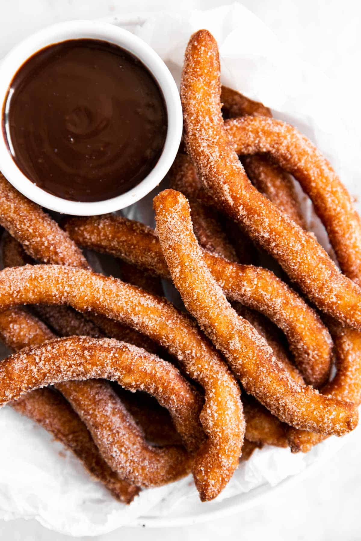 overhead view of homemade churros on white parchment with bowl of chocolate sauce