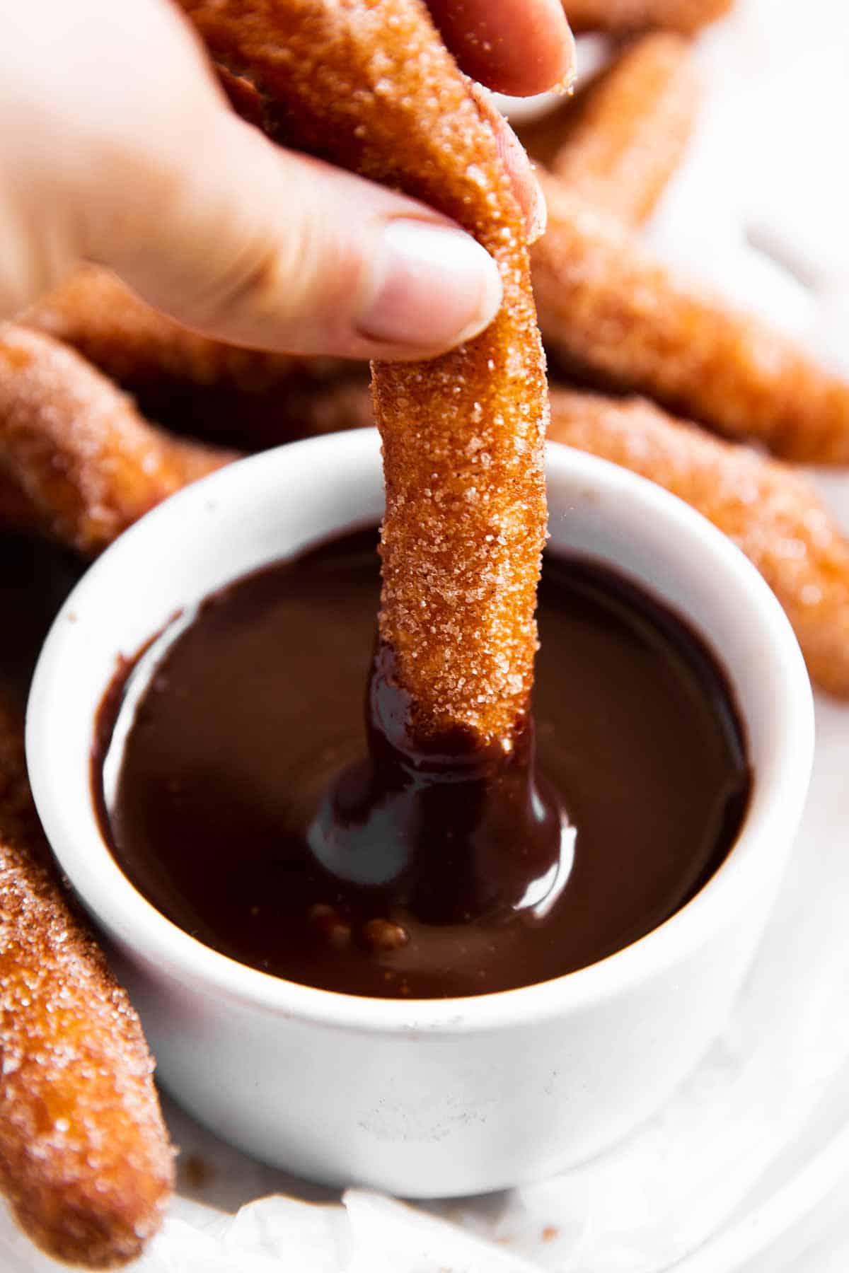 female hand dipping churro into thick chocolate sauce