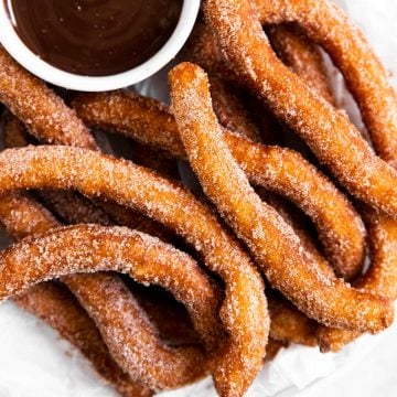 overhead view of homemade churros on white parchment with bowl of chocolate sauce