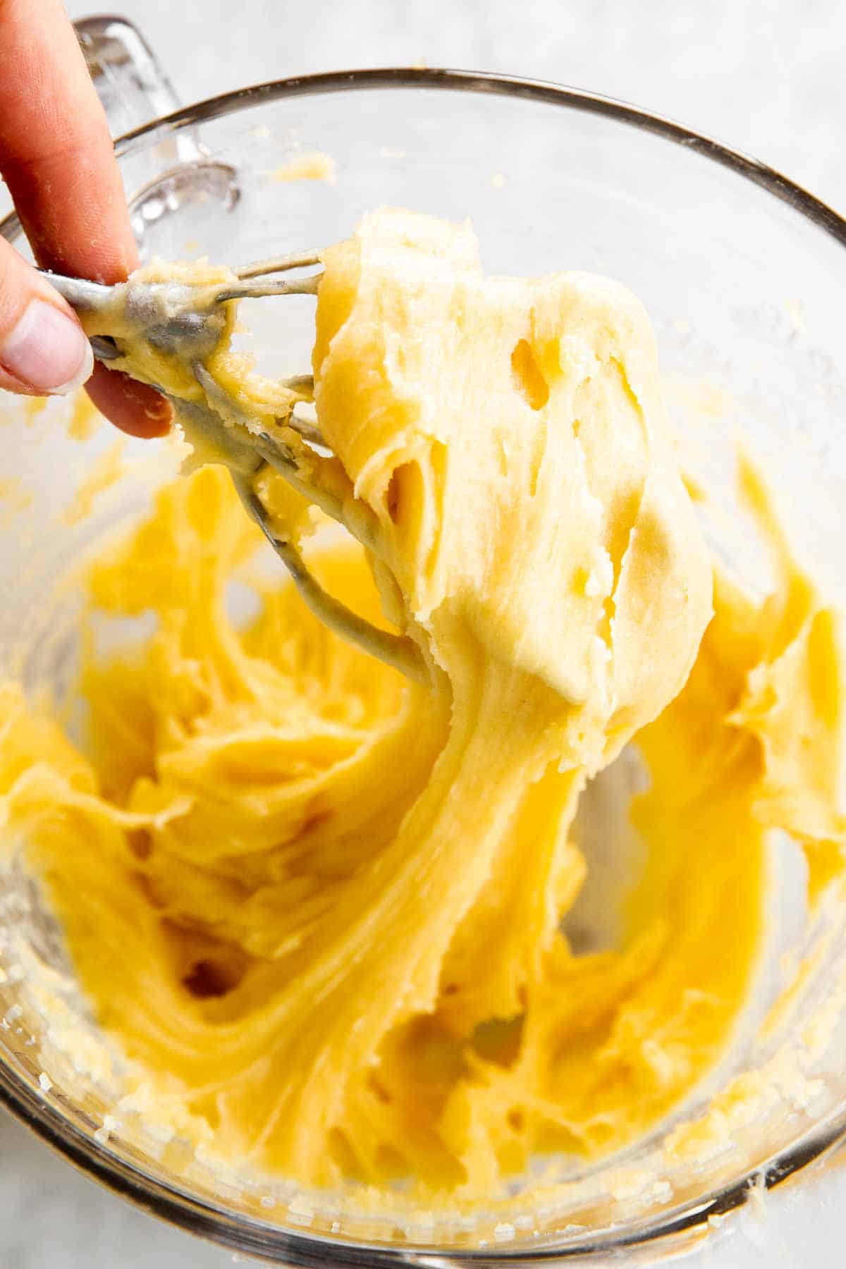 female hand pulling choux pastry from glass bowl with mixer beaters