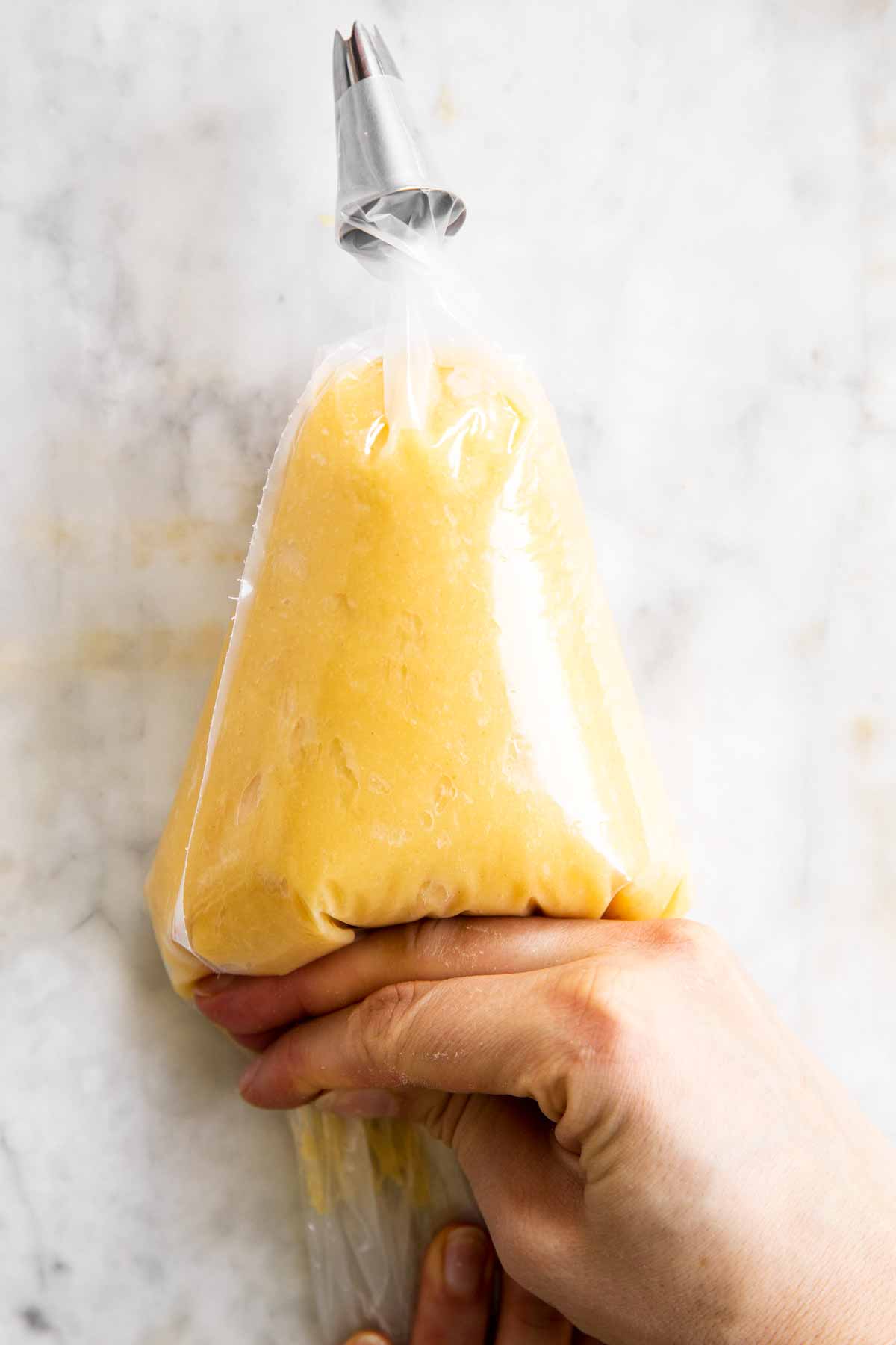 female hand adjusting placement of choux pastry in piping bag