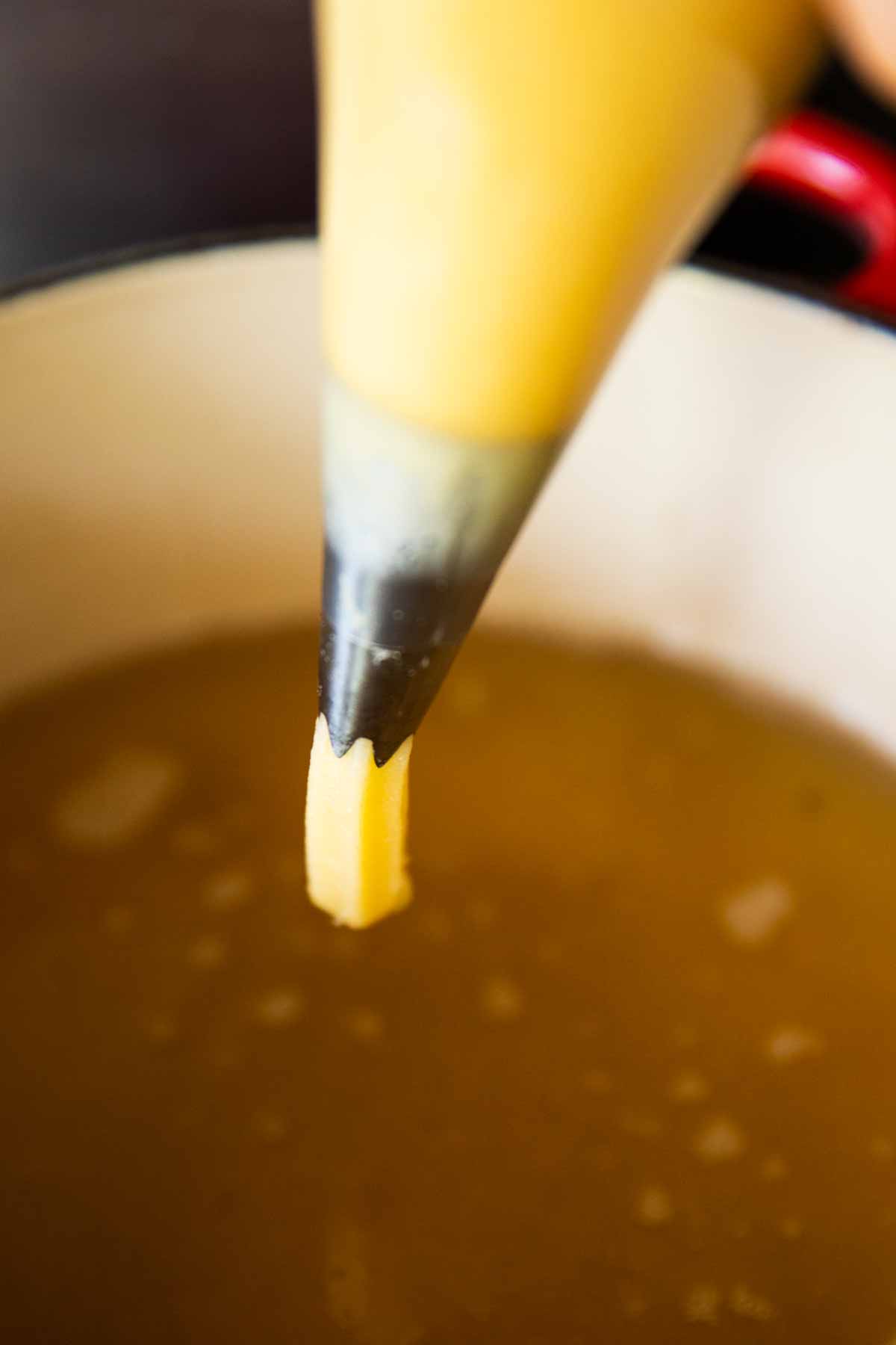 piping bag piping choux pastry over simmering oil