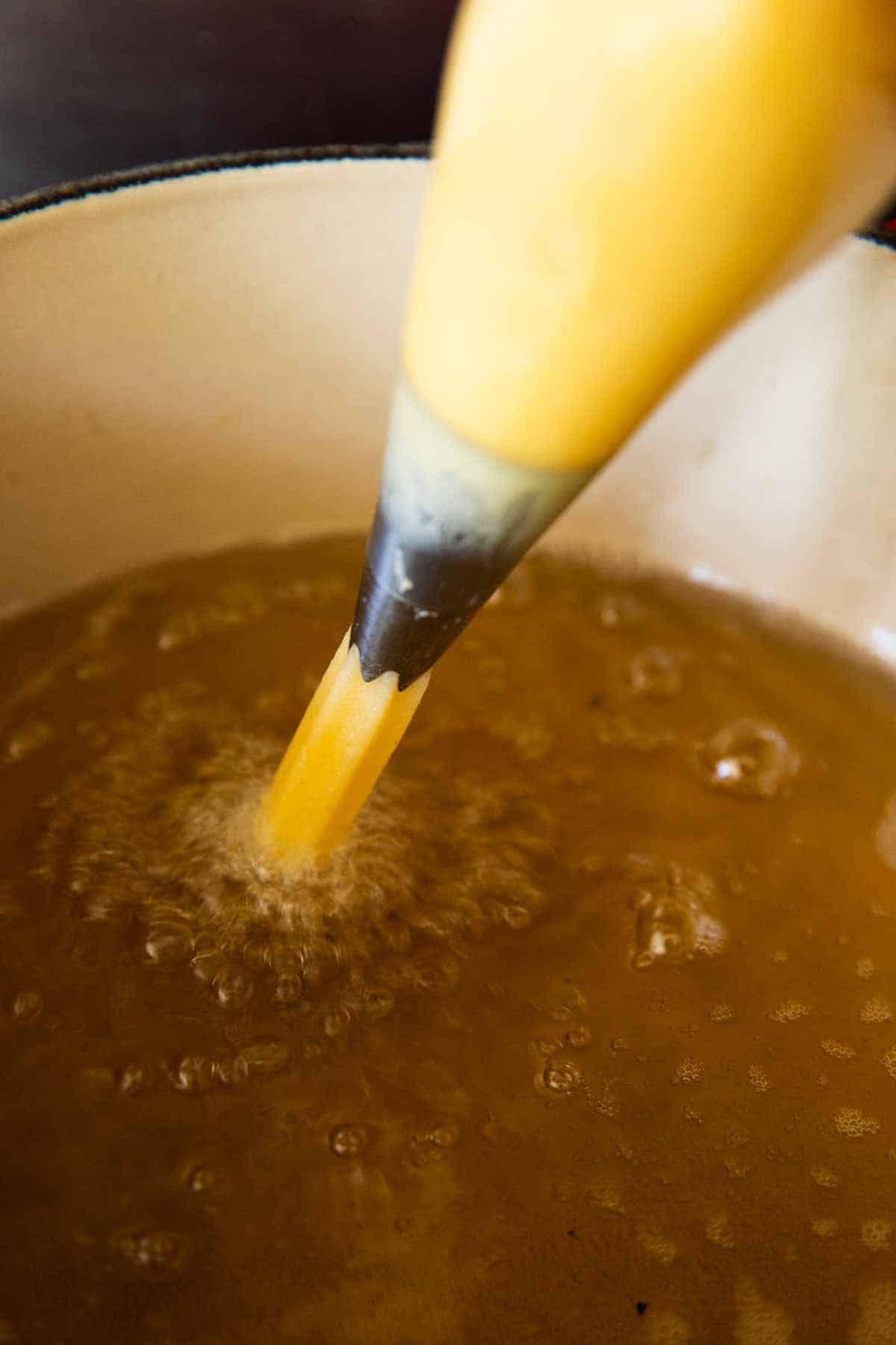 piped choux pastry coming from pastry bag in simmering oil