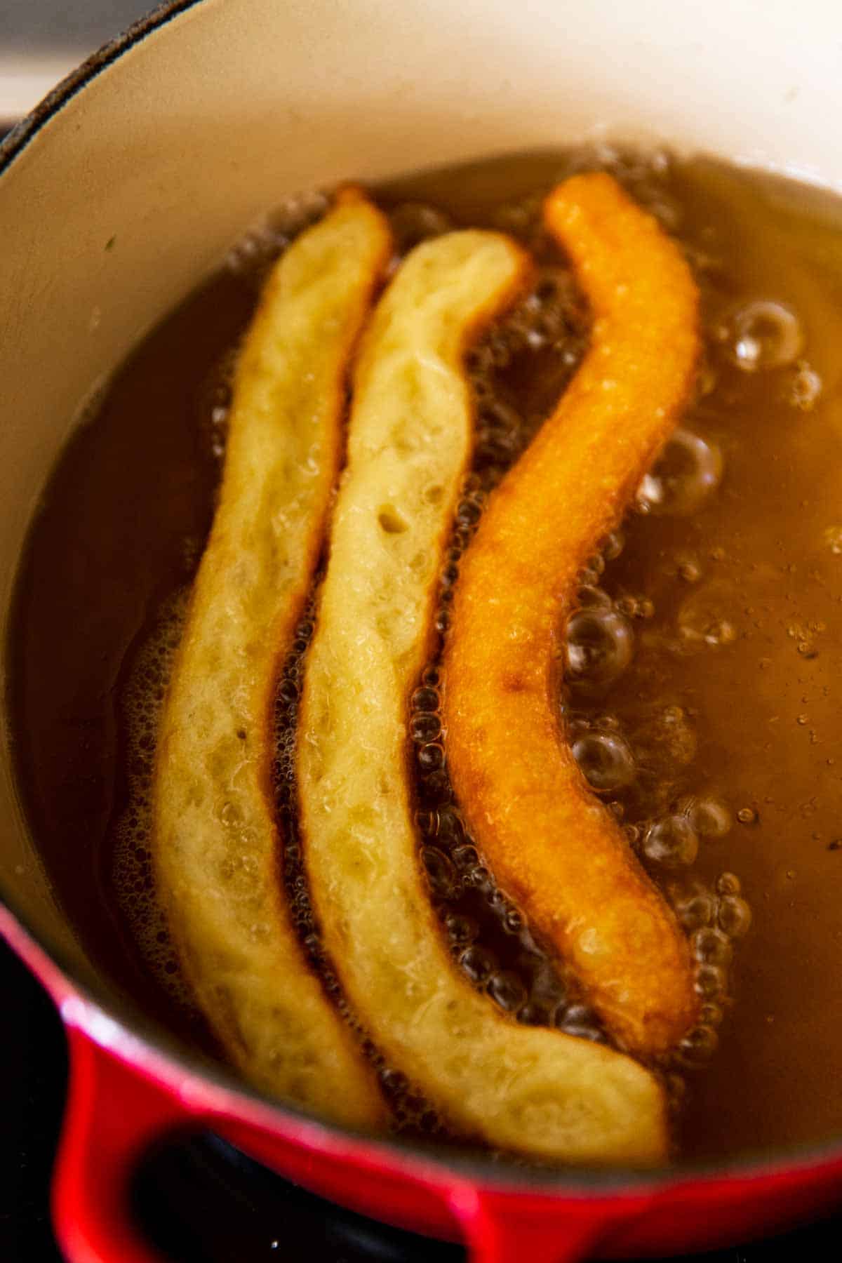 two unflipped churros and one flipped churro in simmering oil