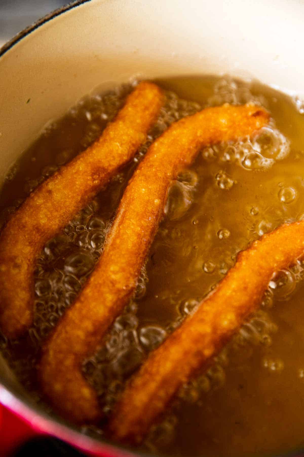 three flipped churros in simmering oil