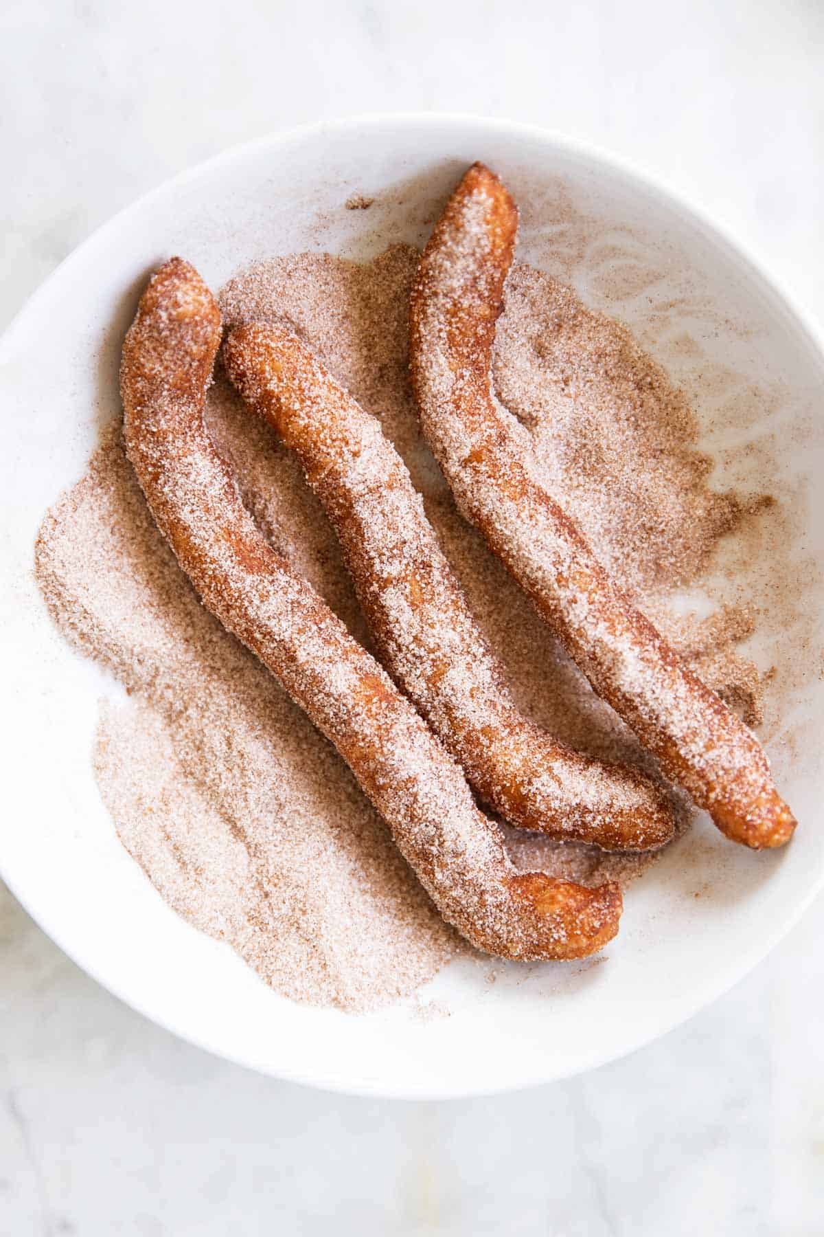 three churros in bowl with cinnamon sugar