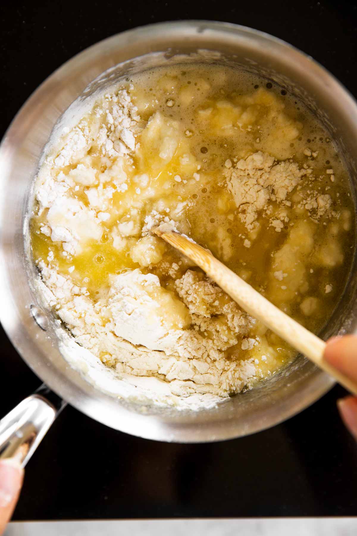 female hand stirring flour in melted butter in saucepan