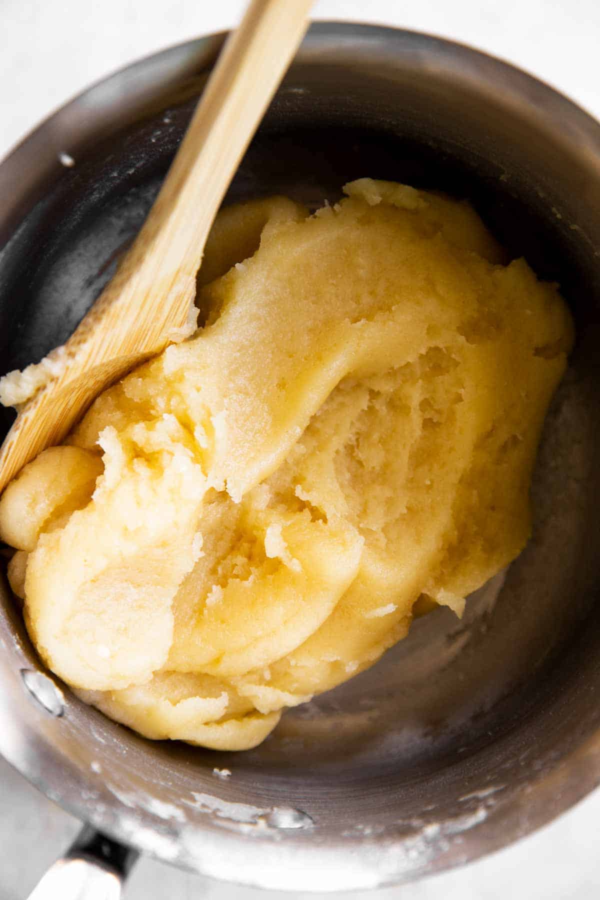close up photo of cooked choux pastry in saucepan with wooden spoon
