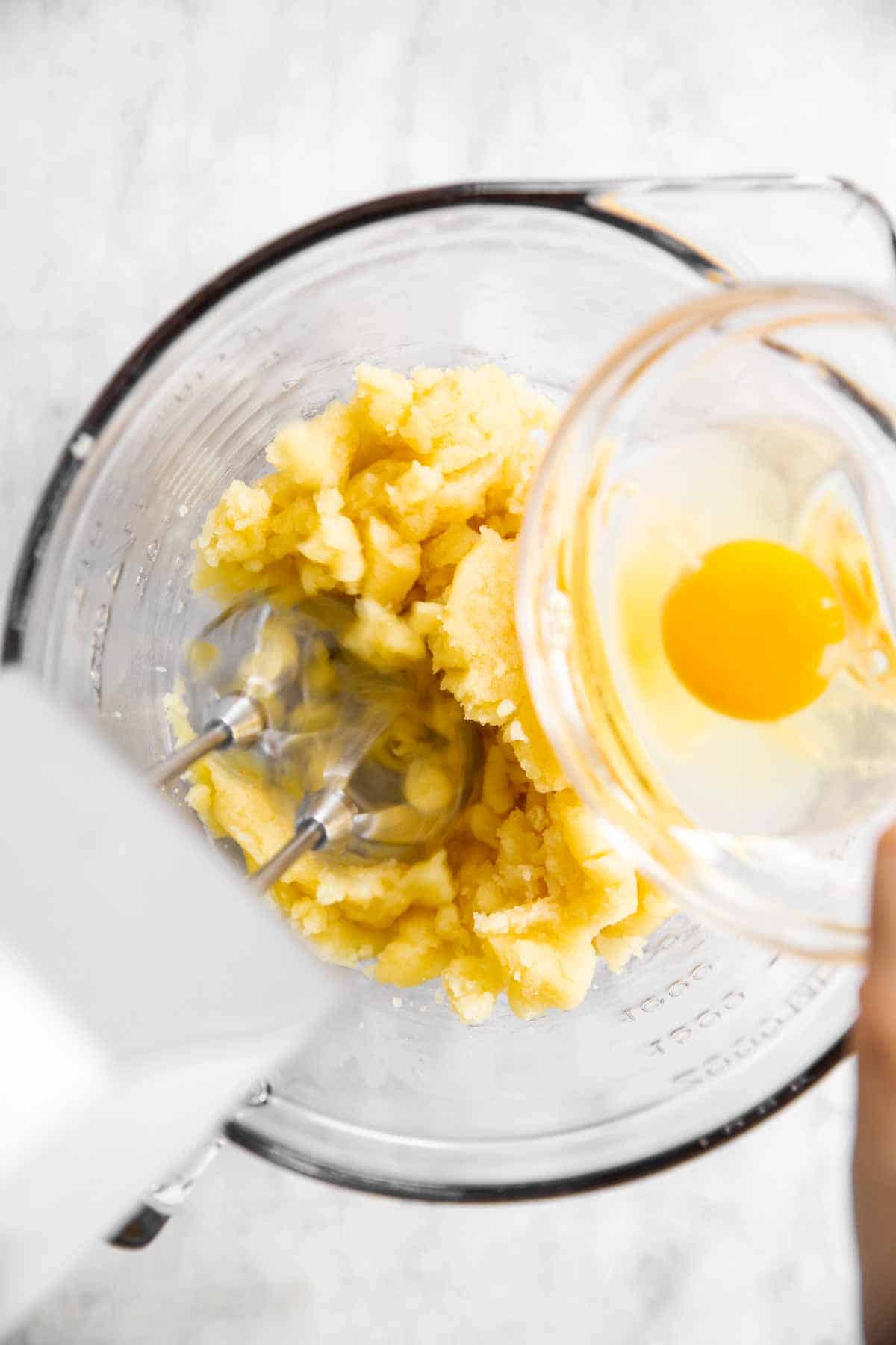 female egg pouring egg from glass prep bowl into mixing bowl with choux pastry