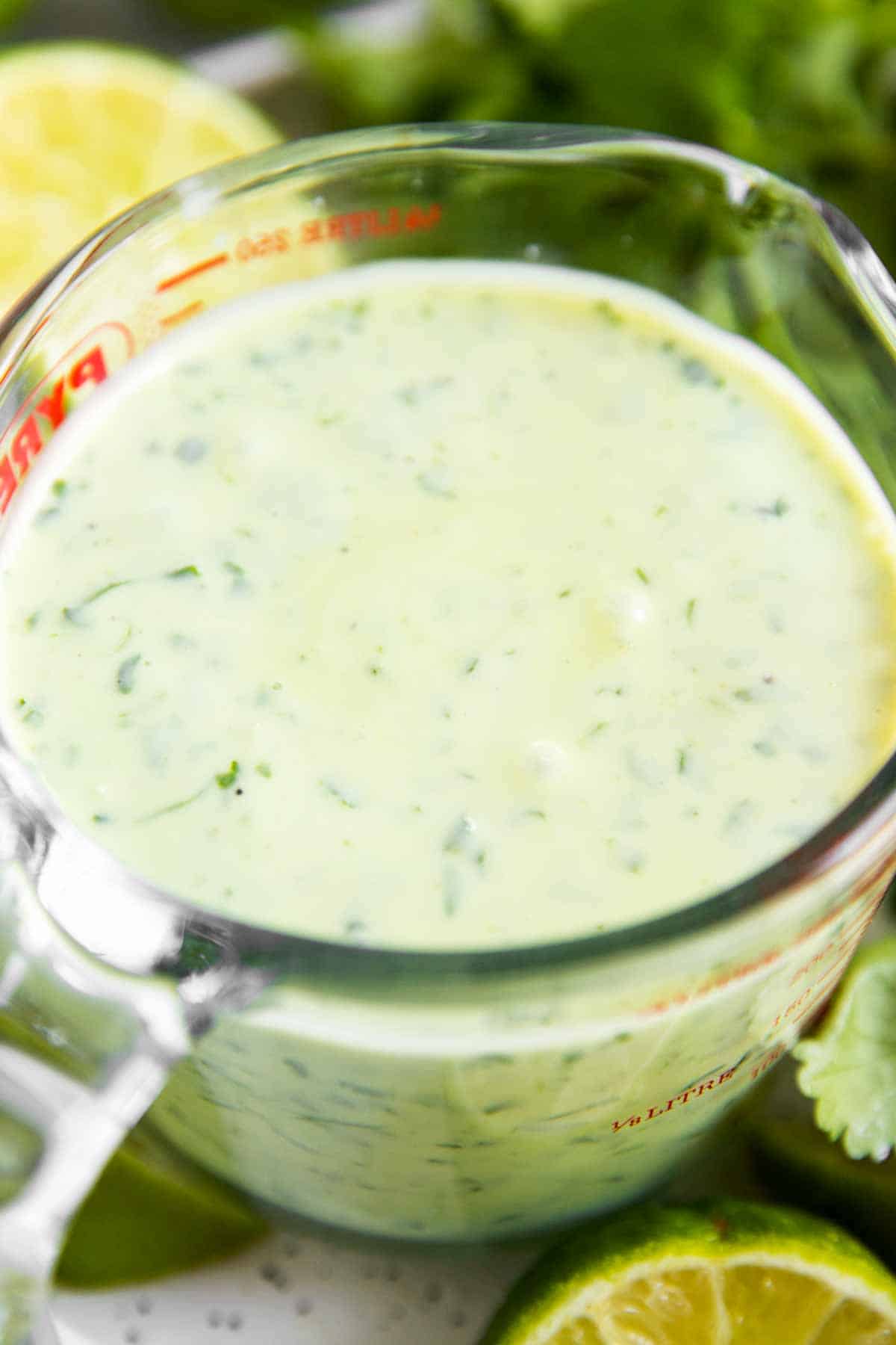 cilantro lime dressing in glass measuring jug surrounded by fresh cilantro and lime