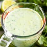 cilantro lime dressing in glass measuring jug surrounded by fresh cilantro and lime