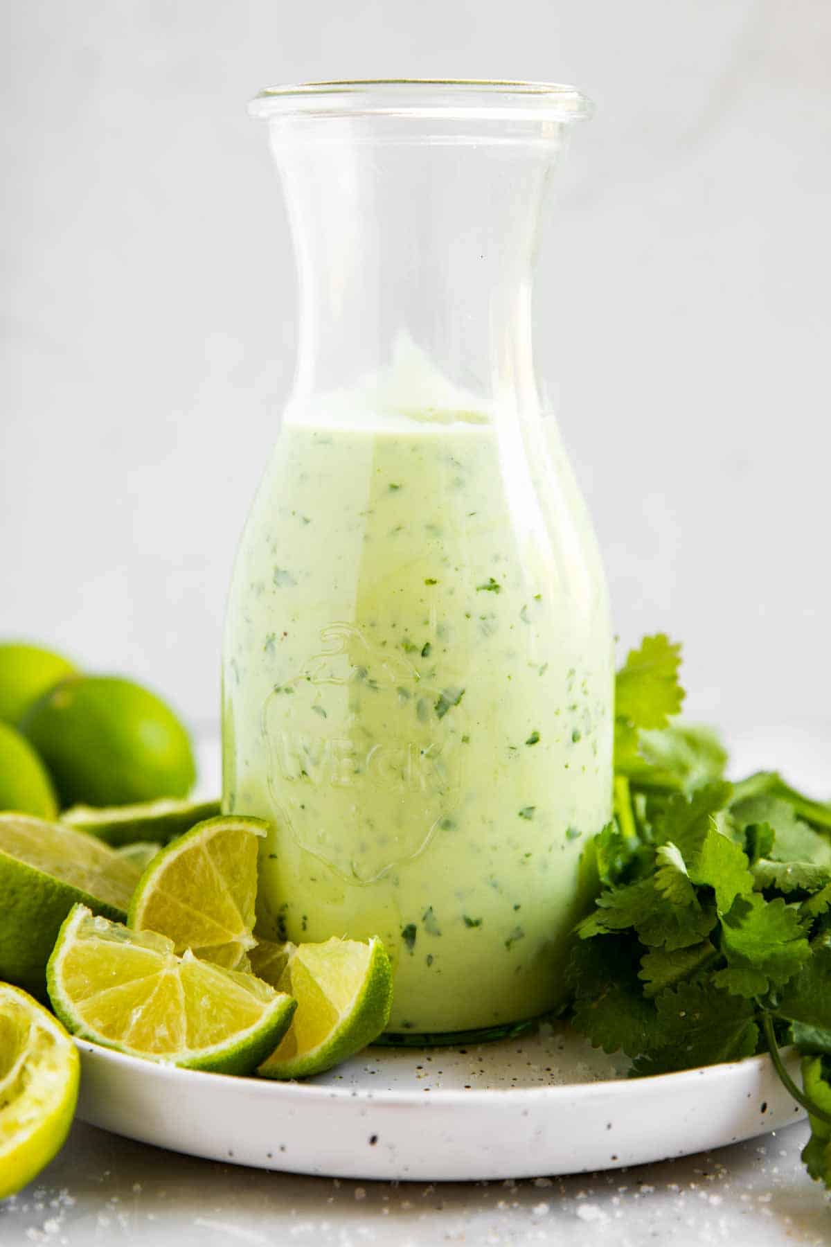 cilantro lime dressing in glass flask on plate with fresh cilantro and lime wedges