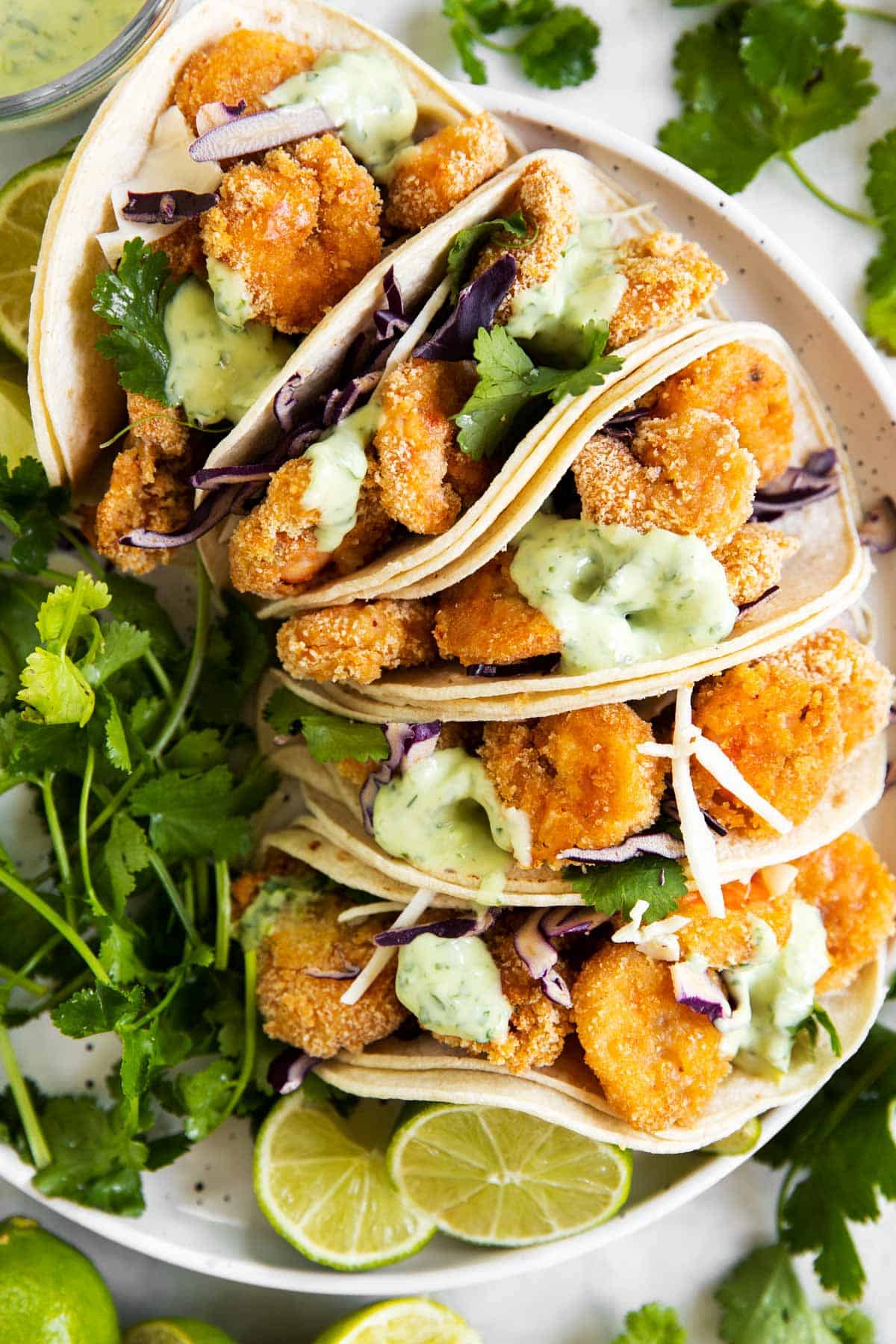 overhead view of five crispy shrimp tacos on white plate with fresh cilantro and lime