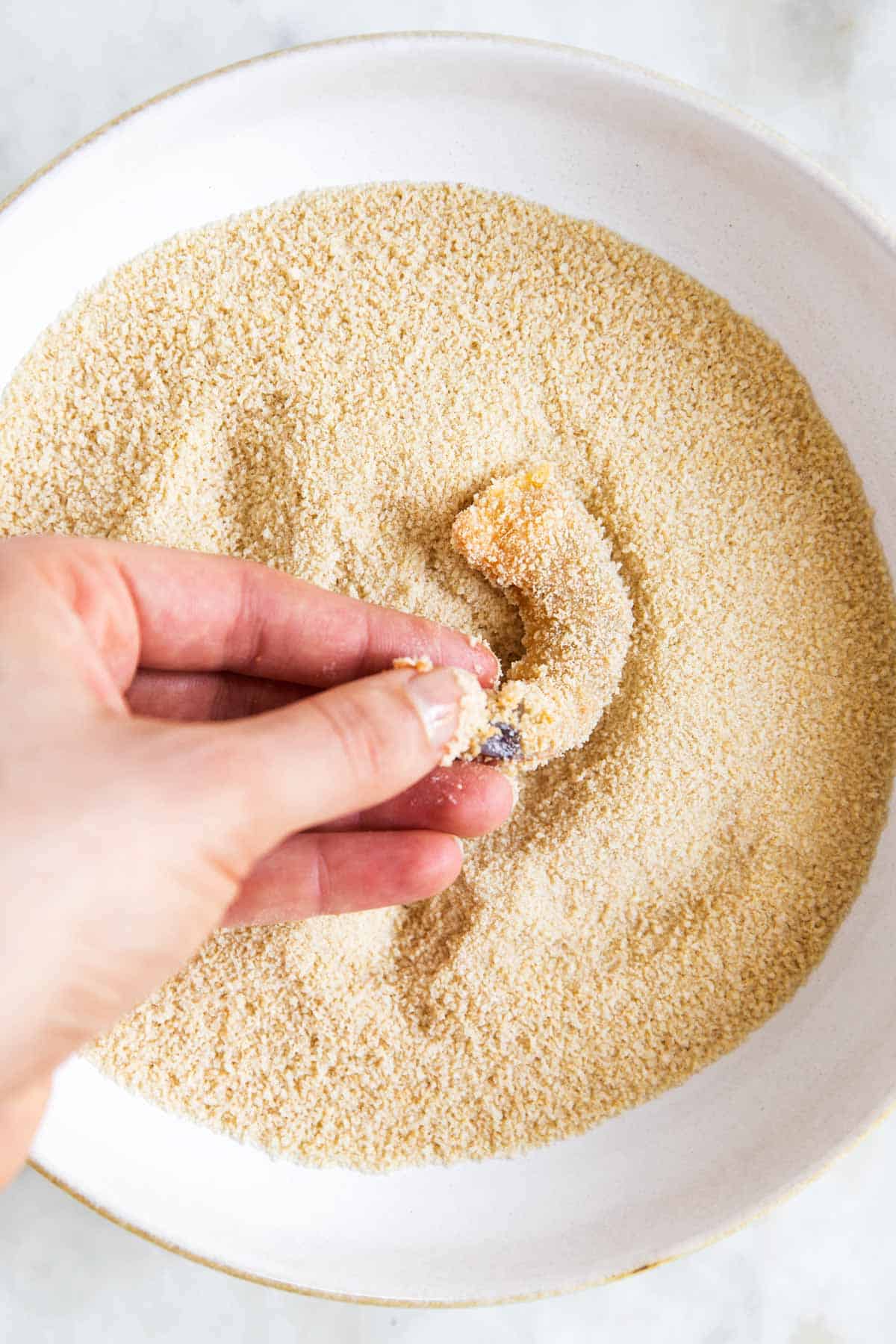 female hand dredging shrimp through breadcrumbs