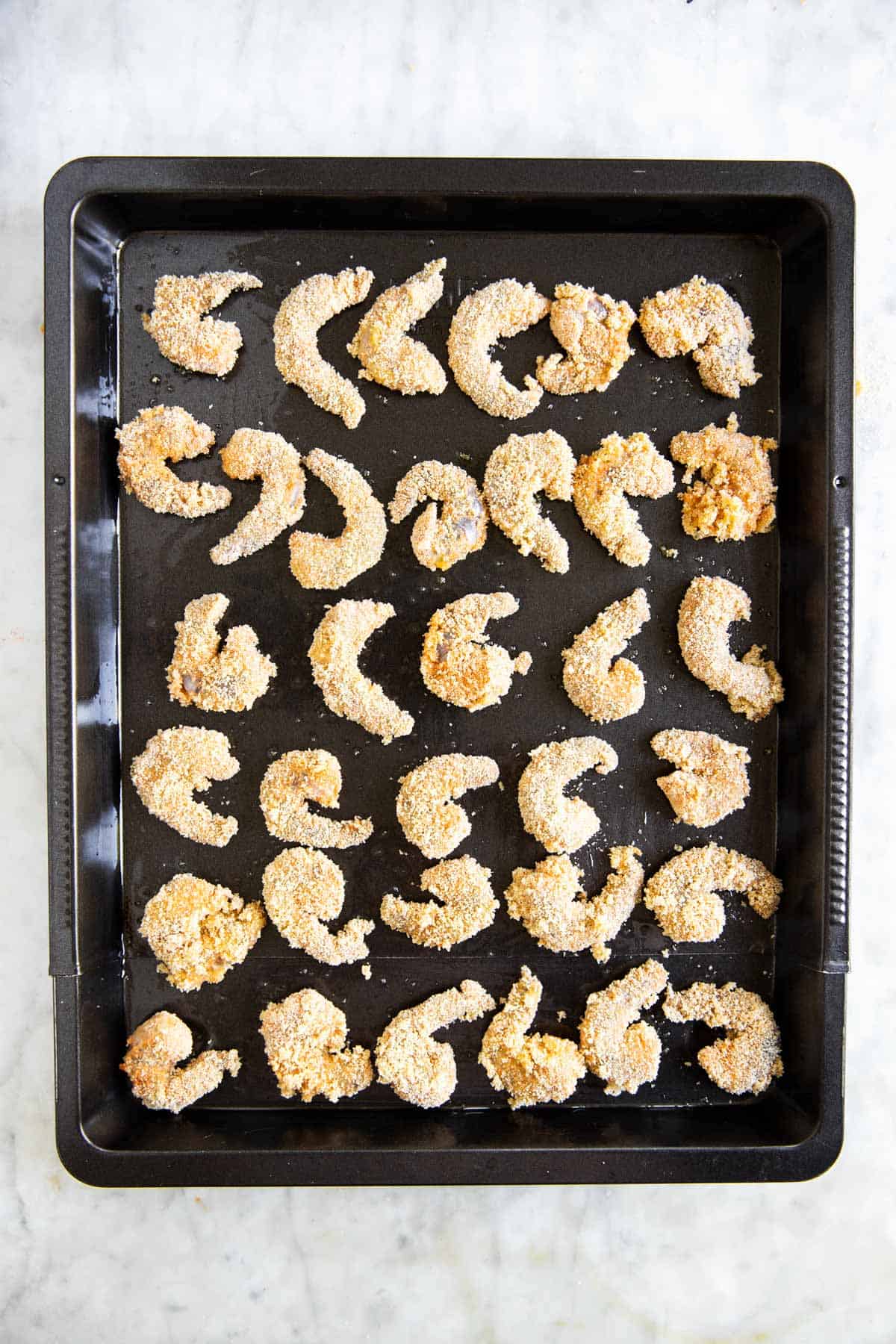 breaded shrimp on dark sheet pan