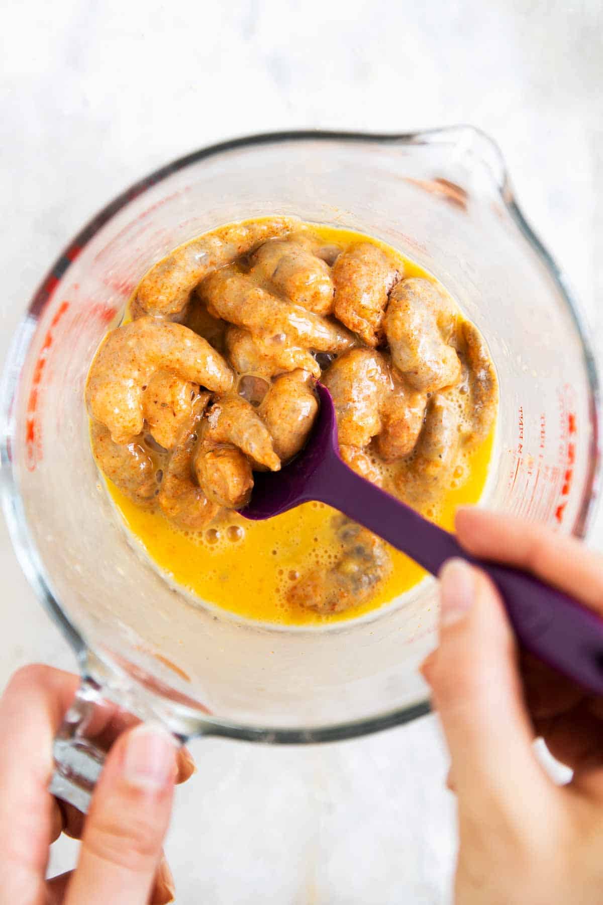 female hand stirring shrimp in egg wash with rubber spatula