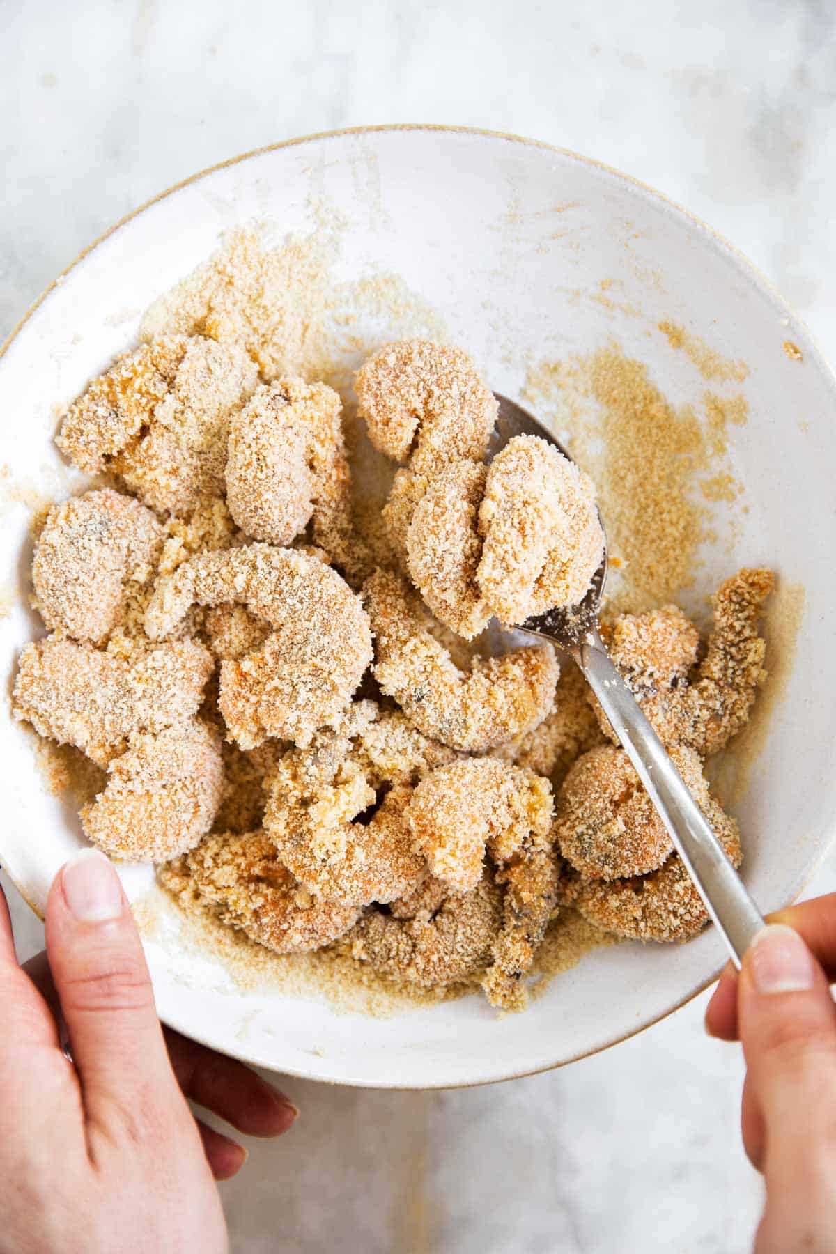 female hand stirring shrimp in white bowl with breadcrumbs