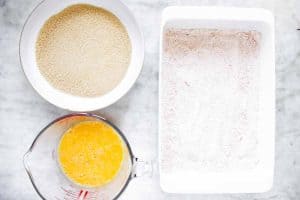 three bowls with ingredients for breading shrimp on marble surface