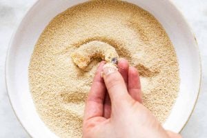 female hand dredging shrimp through breadcrumbs