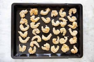 breaded shrimp on dark sheet pan