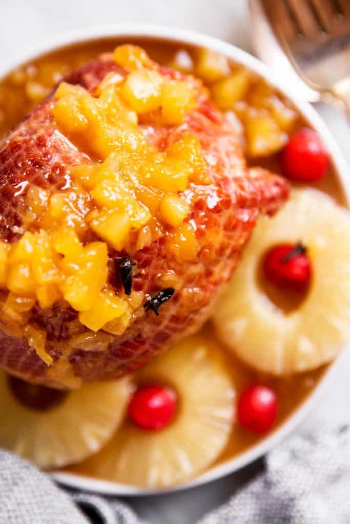 overhead view of pineapple glazed ham on plate with pineapple rings and maraschino cherries