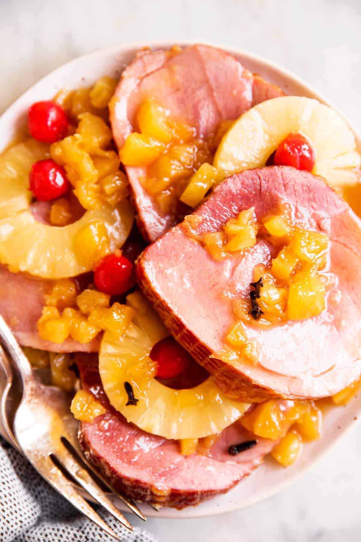 slices of cooked ham with pineapple rings and maraschino cherries on white plate