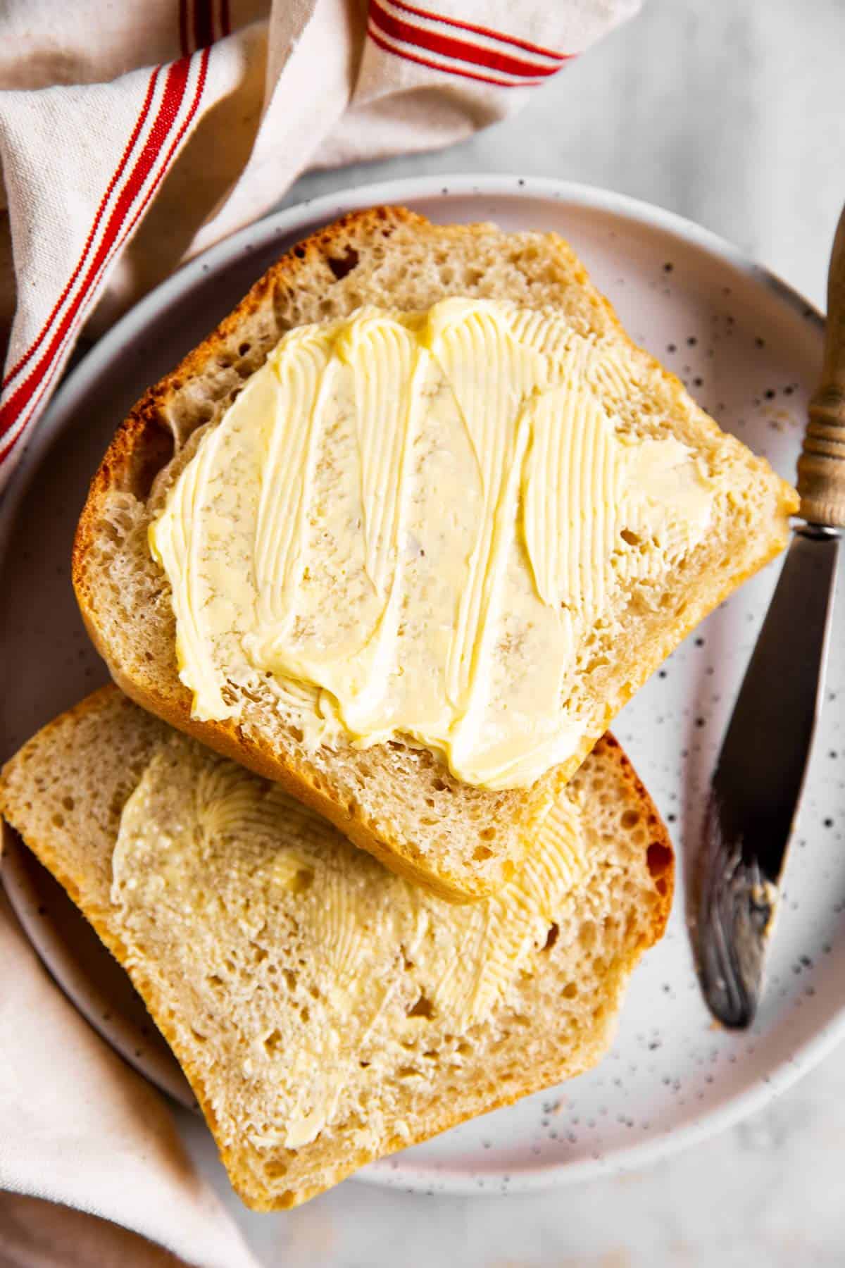 two buttered slices of sourdough bread on white plate next to white and red kitchen towel