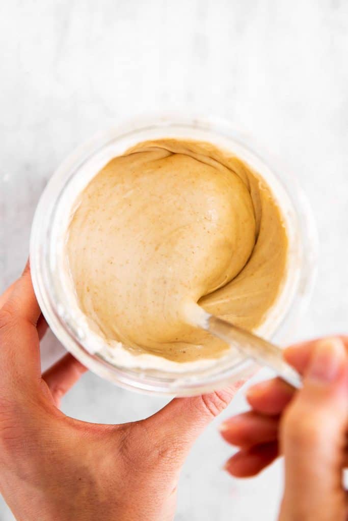 female hands stirring sourdough starter I'm glass jar with a fork