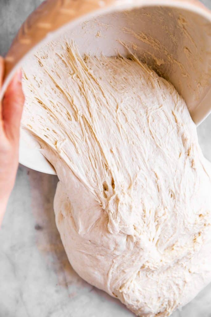 female hand removing sourdough from bowl to marble surface