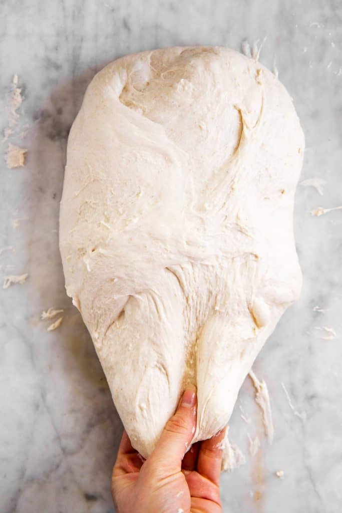 female hand stretching sourdough on marble surface