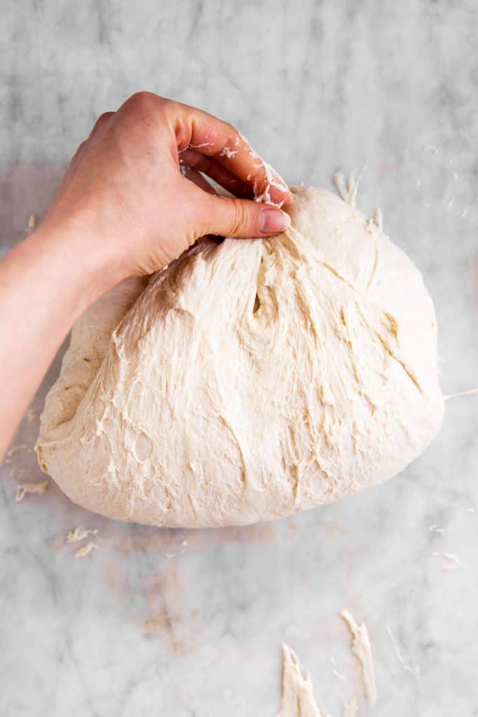 female hand folding sourdough on marble surface